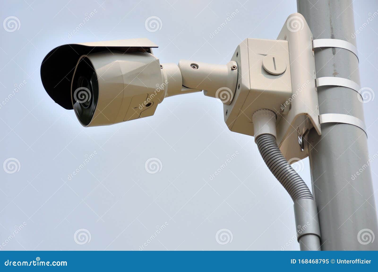 a public surveillance camera installed on a lamp post against a light hazy cloudless blue sky