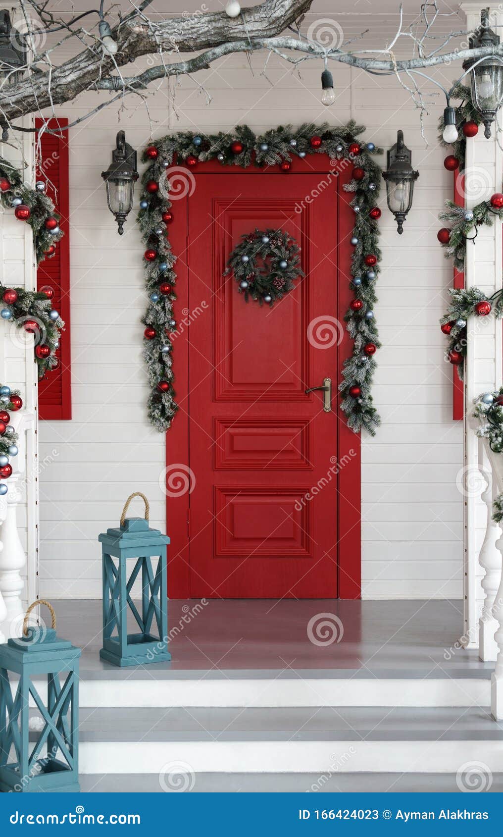 Puerta roja decorada para las fiestas navideñas con farolillos azules en las escaleras