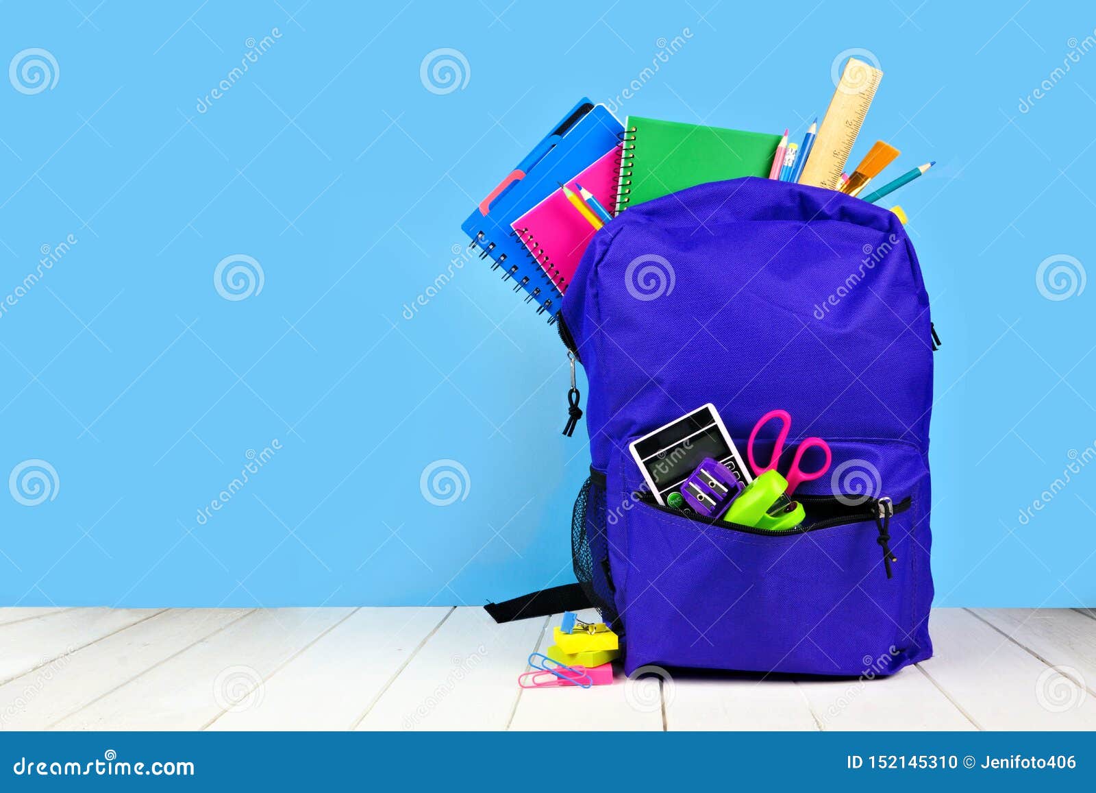 purple backpack full of school supplies against a blue background. back to school.