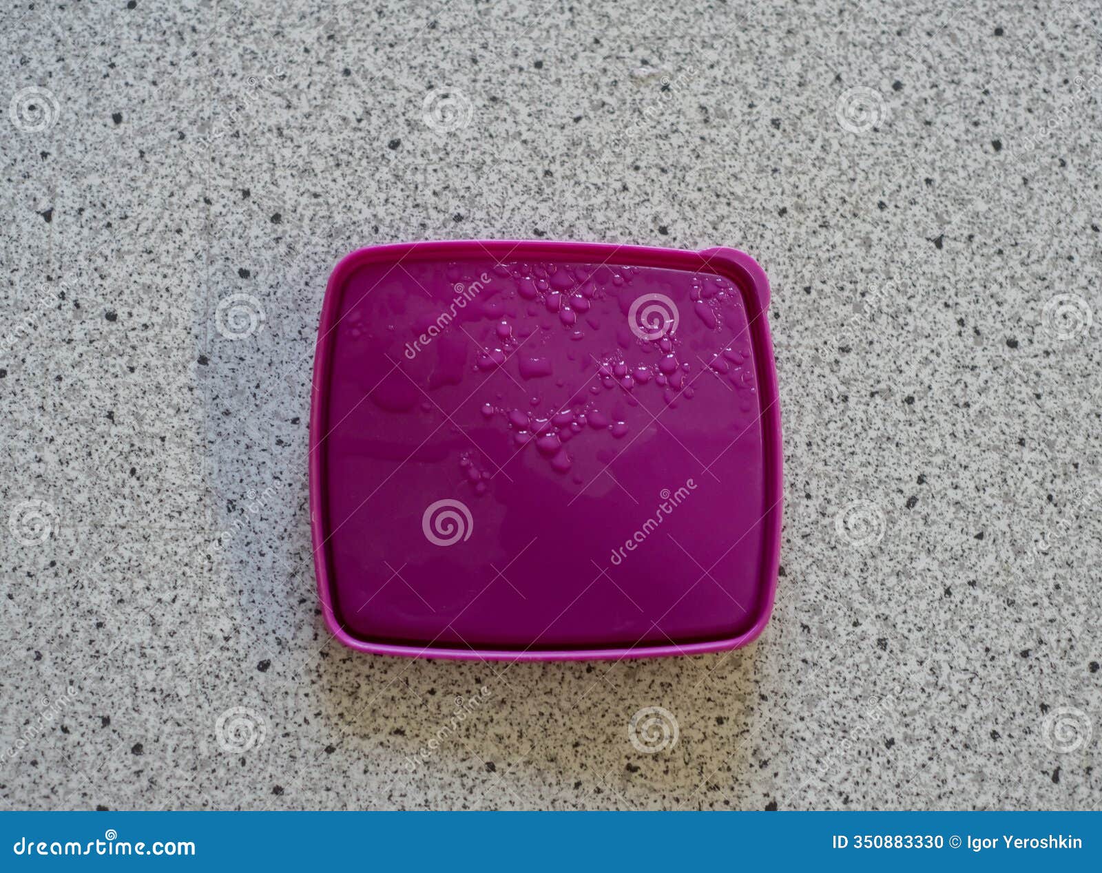 purple plastic lid with water droplets scattered across smooth surface, lying on textured countertop