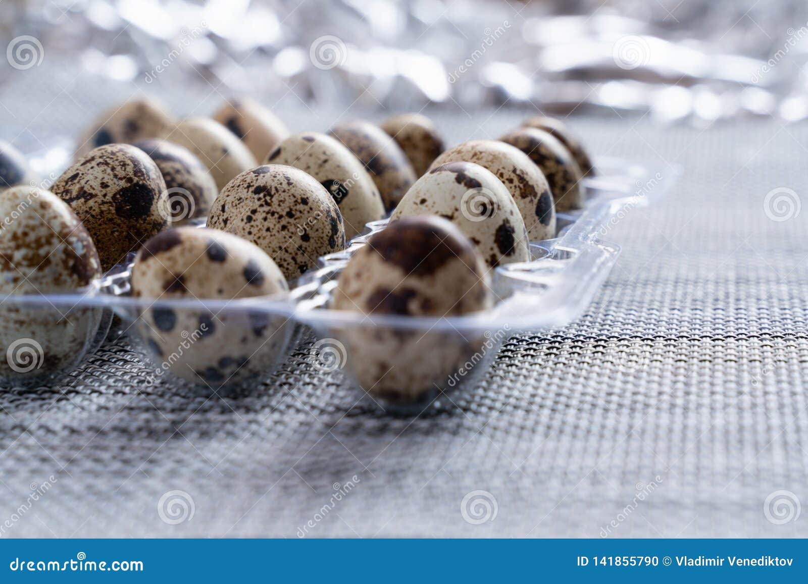 Quail Eggs in a Clear Plastic Container on a Grey Cloth Table Stock