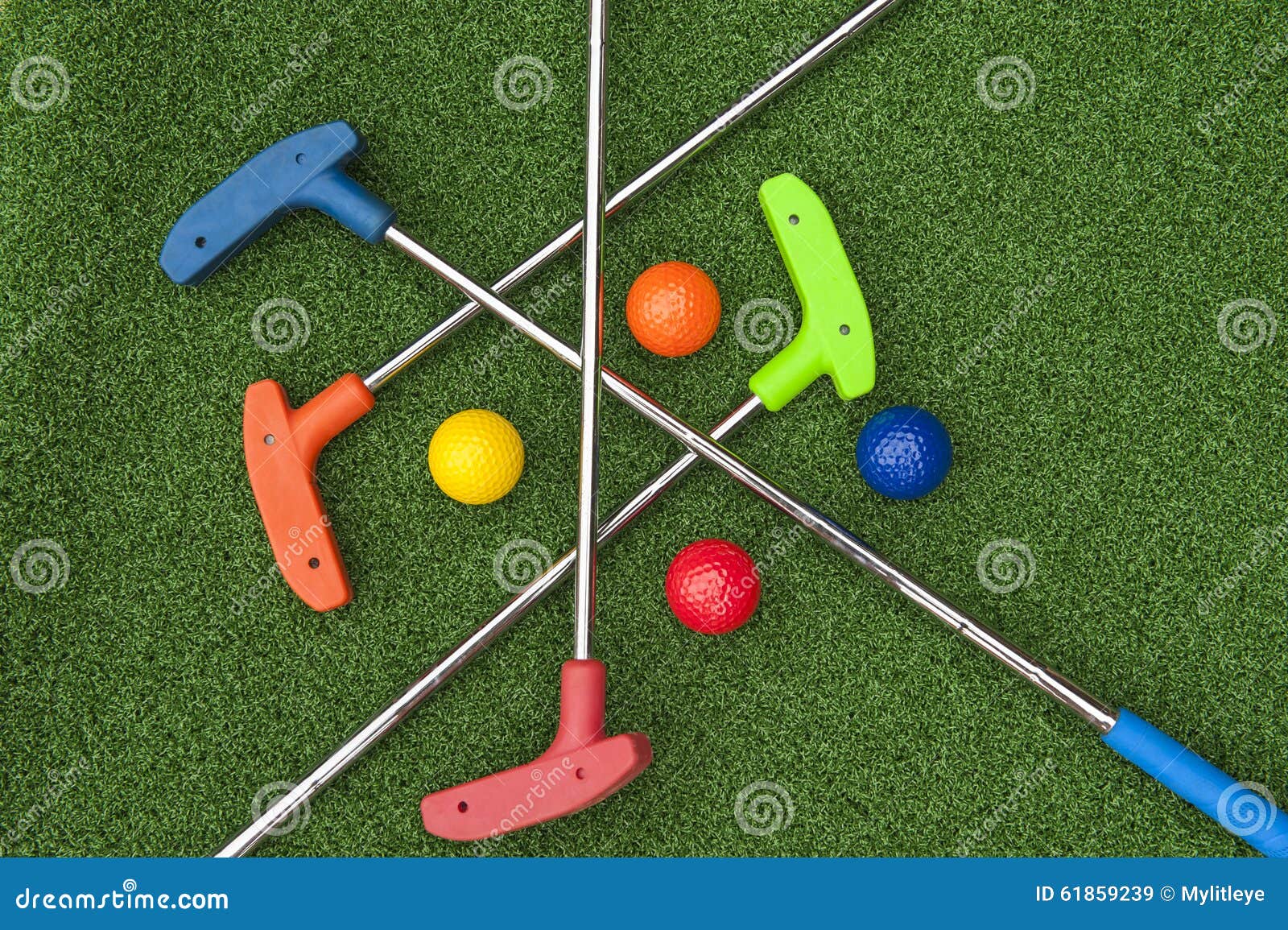 Quatro Mini Golf Putters e bolas. Quatro mini embocadores do golfe e bolas das cores sortidos que colocam criss cruzaram-se na grama artificial