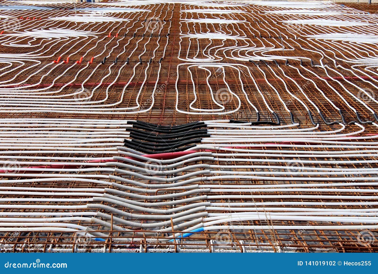 radiant floor heating system being installed at building construction site with densely laid plastic water pipes on top of rusted