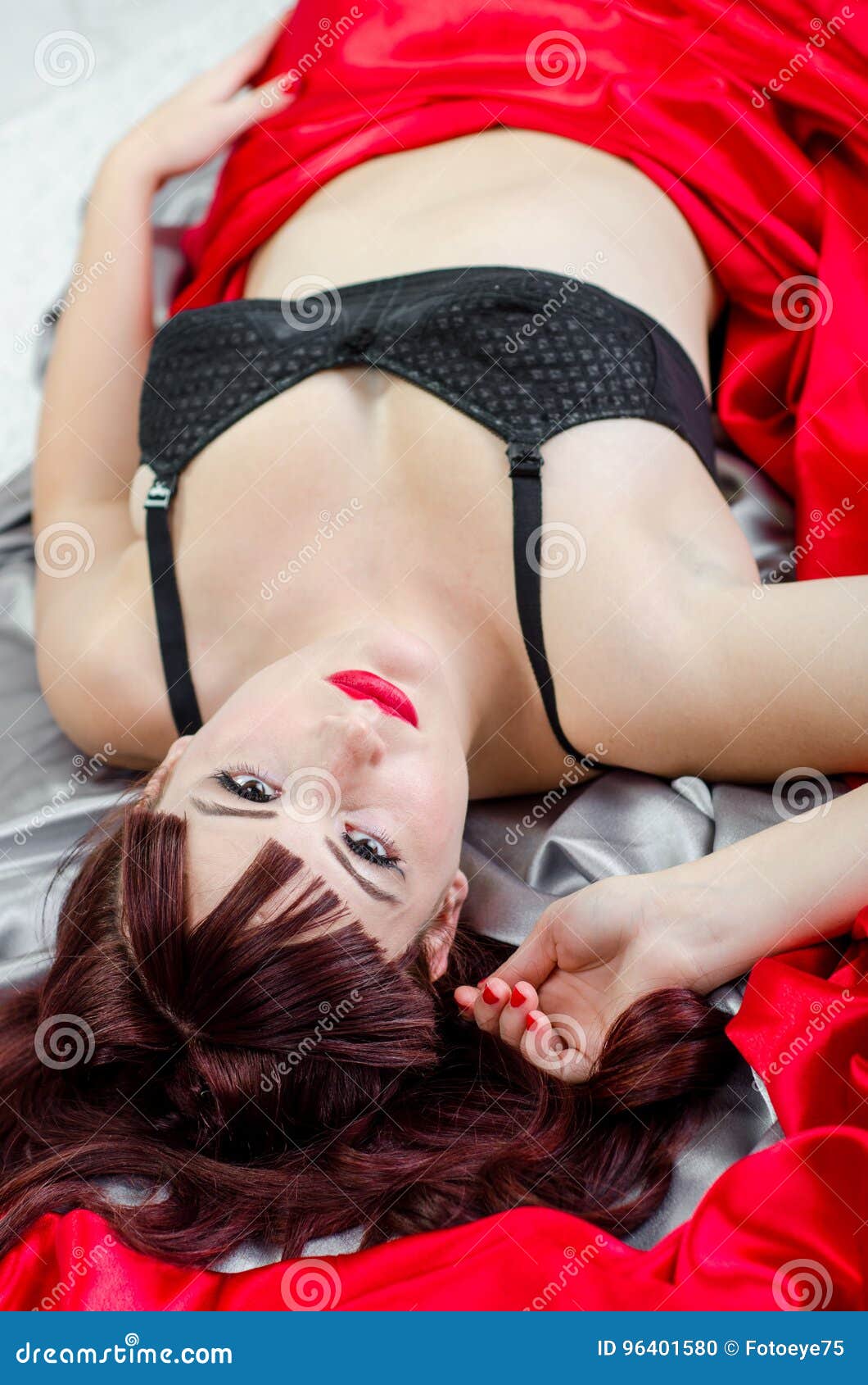 Ragazza sexy del pinup della testarossa. Retro donna rossa sexy del boudoir del pinup dei capelli 50s in vestaglia della biancheria Il modello ha pelle molle leggera, rossetto rosso ponendo a letto sugli strati della seta del raso