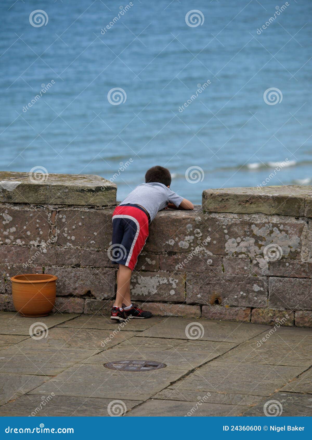 Ragazzo che guarda fuori al mare. Un giovane ragazzo esamina fuori sopra una parete il mare qui sotto.