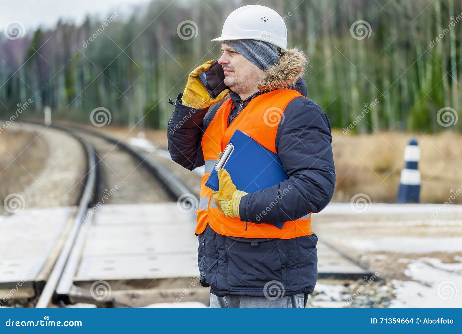 railroad worker with documentation and smartp hone on railway crossing