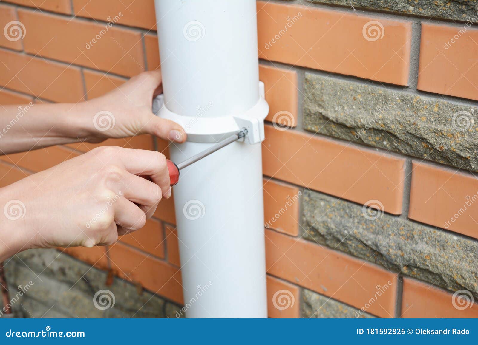 rain gutter installation: a man is screwing the downpipe bracket, socket clip with a screwdriver to fix the downspout to the wall