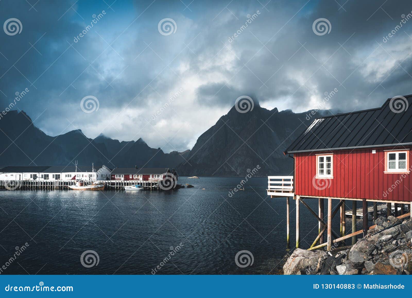 rainbow ofer red houses rorbuer of reine in lofoten, norway with red rorbu houses, clouds, rainy blue sky and sunny