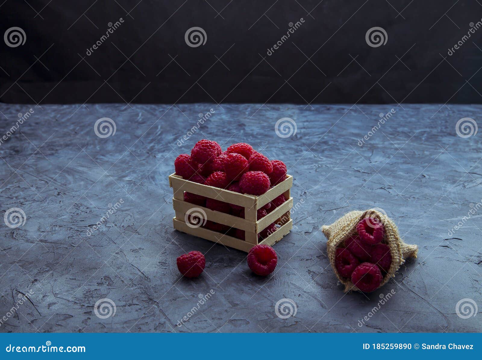 raspberries in red color in a small wooden box and with a jute sack filled with the same fruit