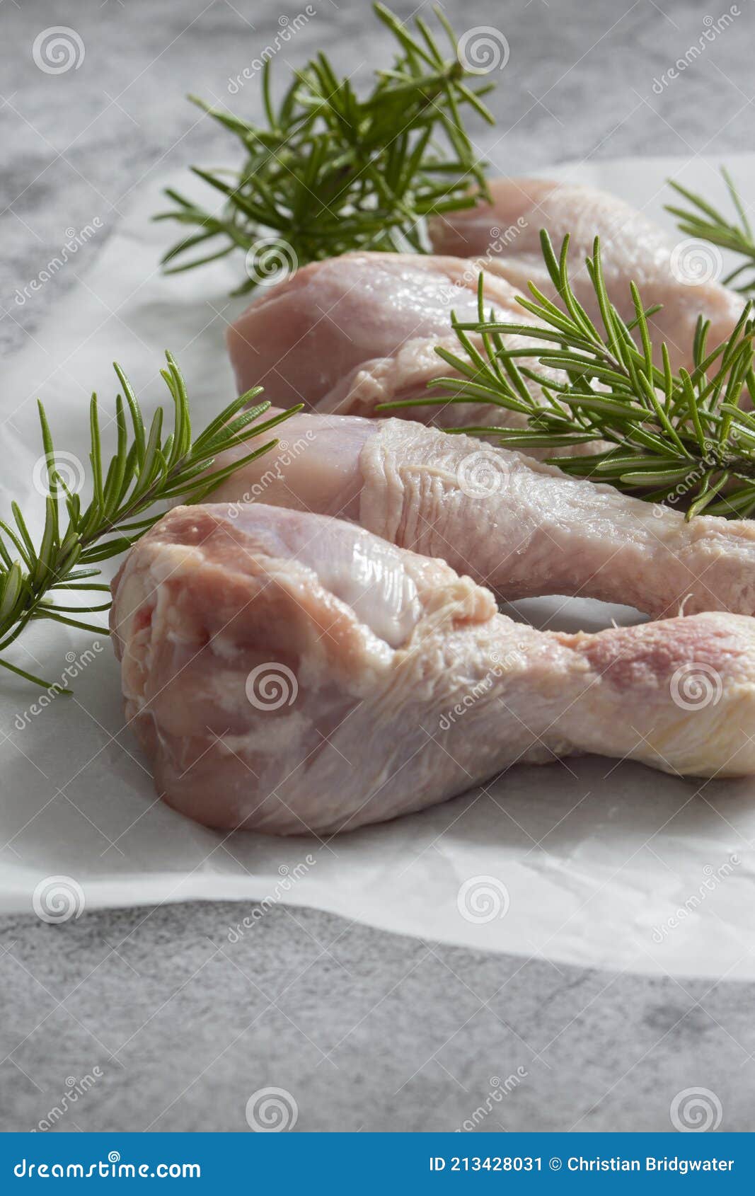 raw chicken drumsticks with rosemary on greaseproof paper.