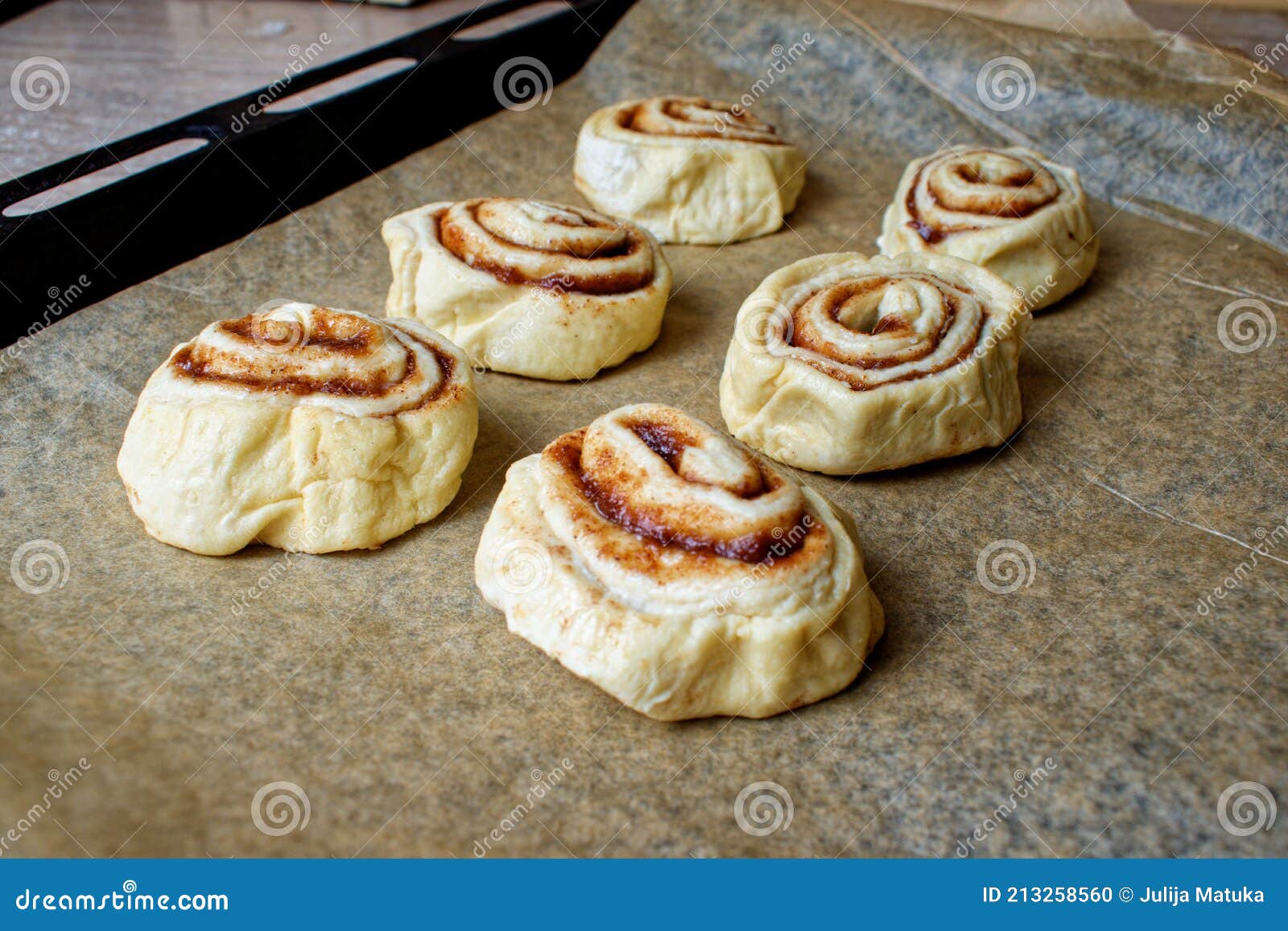 Raw Cinnamon Rolls on a Pan. Six Defrosted Buns on Baking Paper Stock