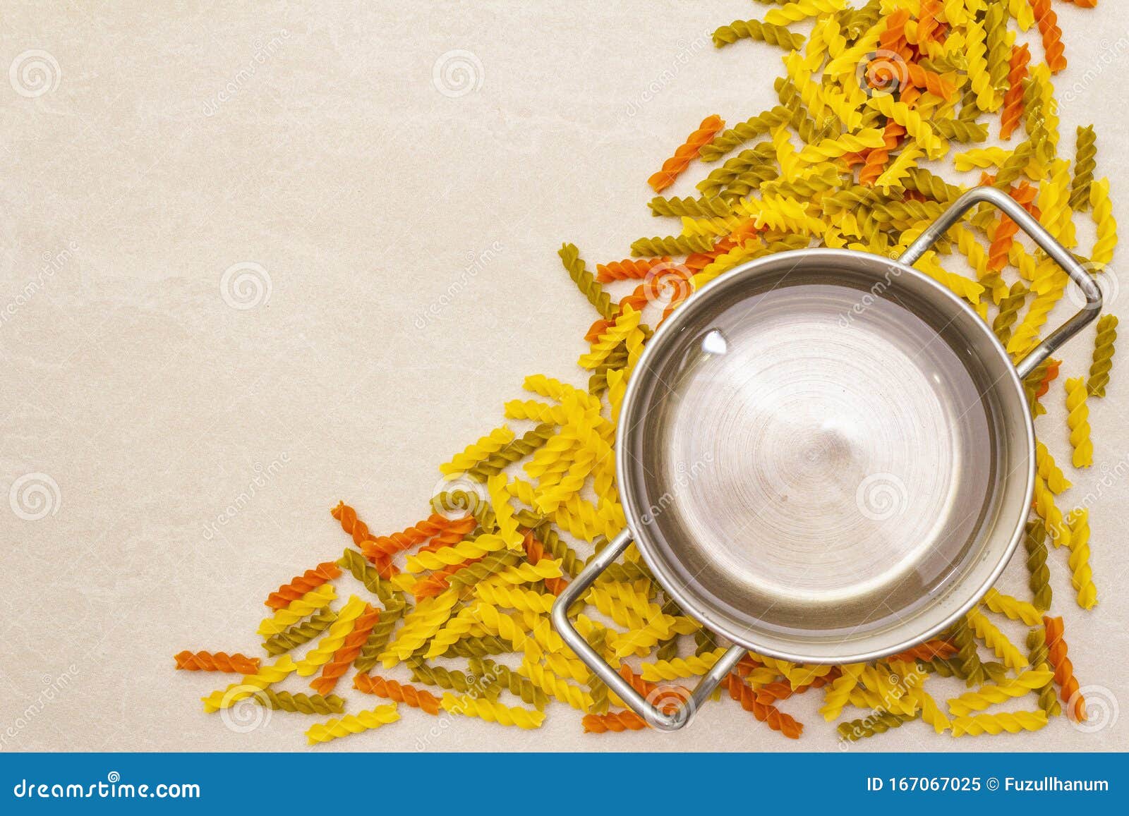 raw fuzilli with water in pot. multicolored pasta scattered over stone background. preparing for children