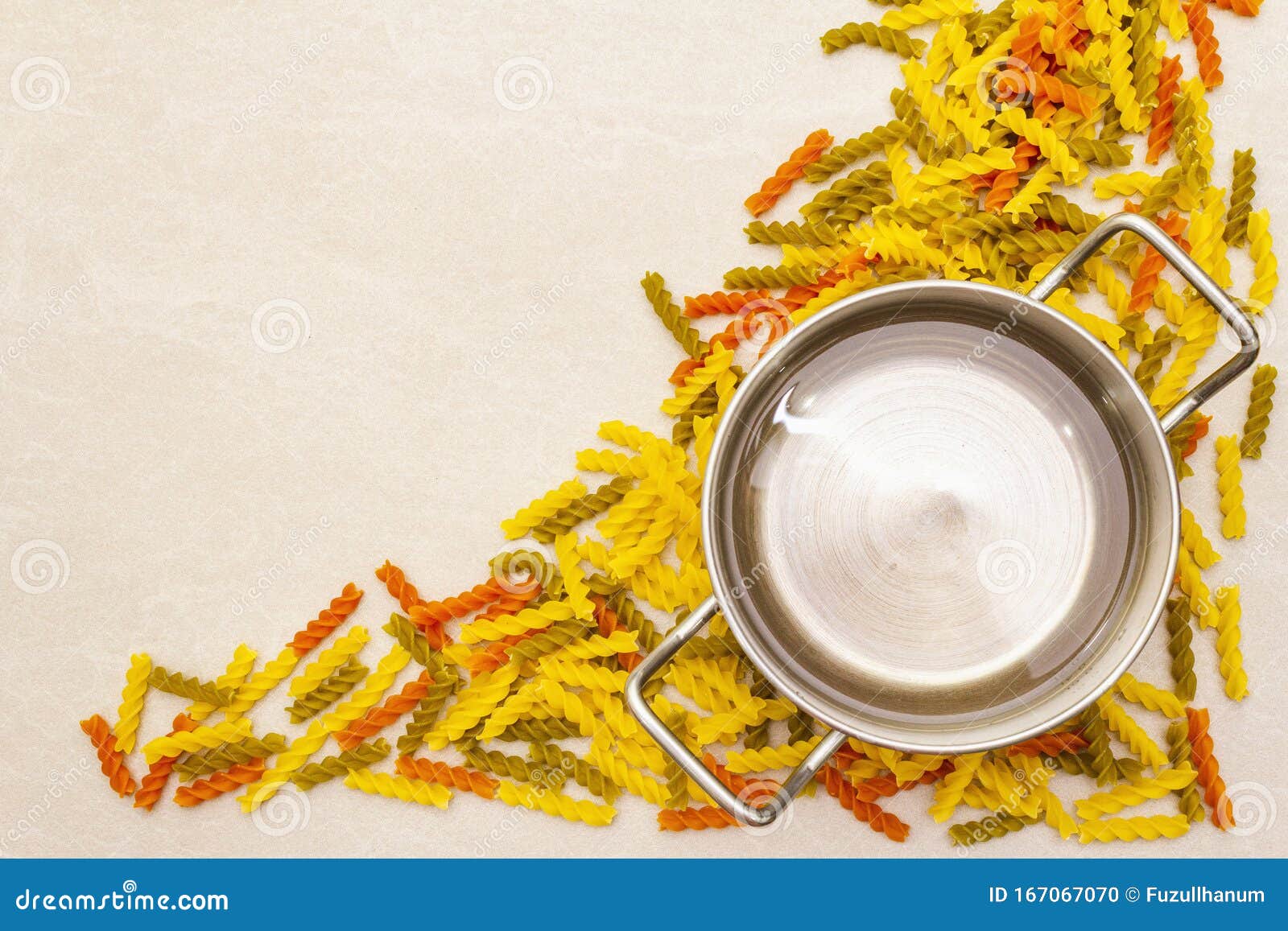 raw fuzilli with water in pot. multicolored pasta scattered over stone background