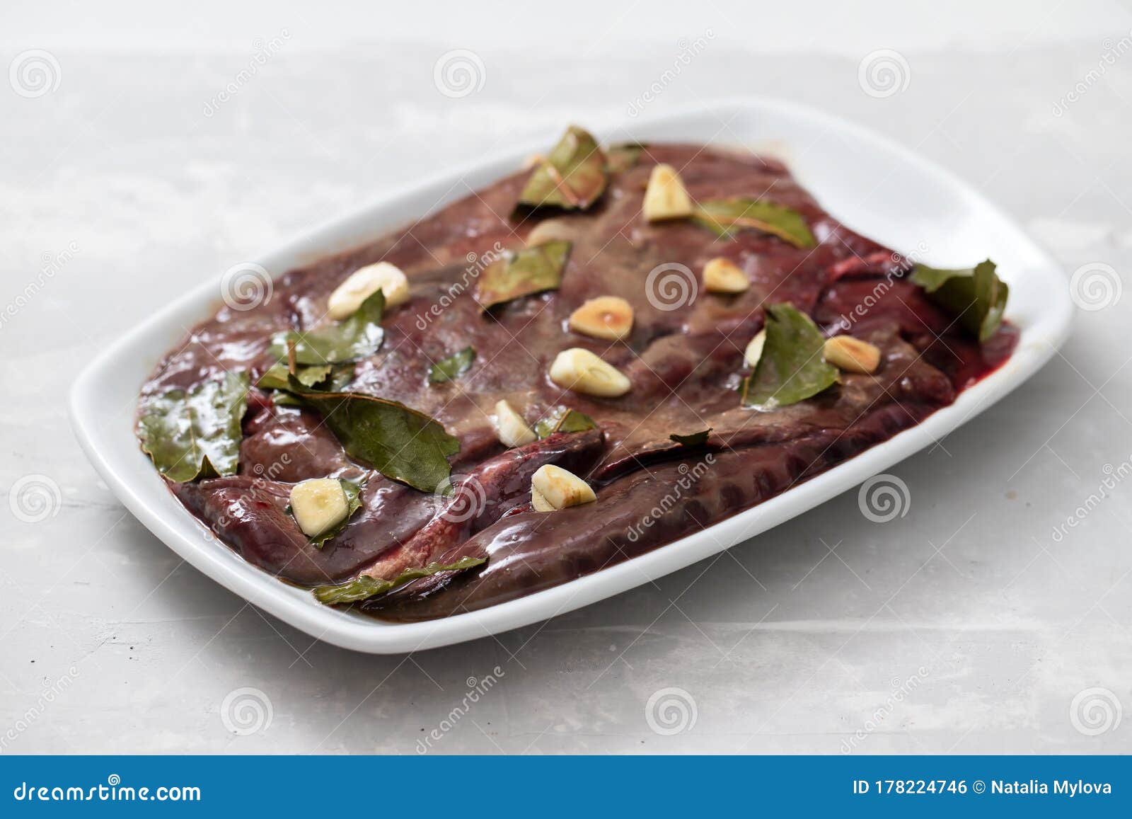 Raw Liver with Garlic and Bay Leaf on White Dish on Ceramic Background
