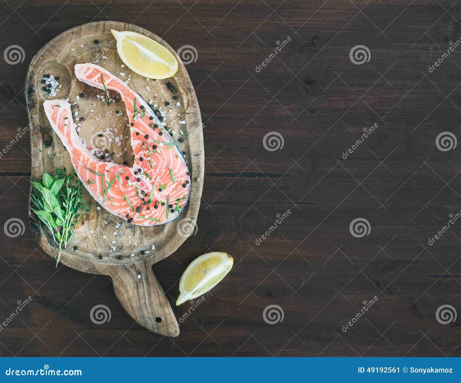 raw salmon steak with fresh herbs, lemon and spices on rustic wooden board over a dark woog background with a copy space
