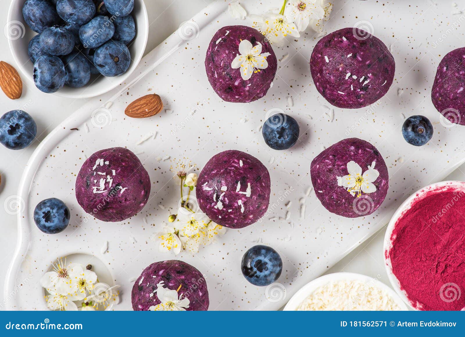 raw vegan energy bites or balls made of blueberry, acai, nuts and dates served with flowers. top view. food styling