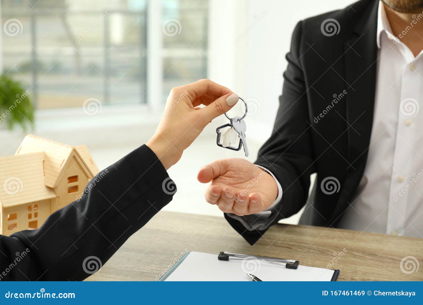 Real Estate Agent Giving Key To Client at Table in Office Stock Image
