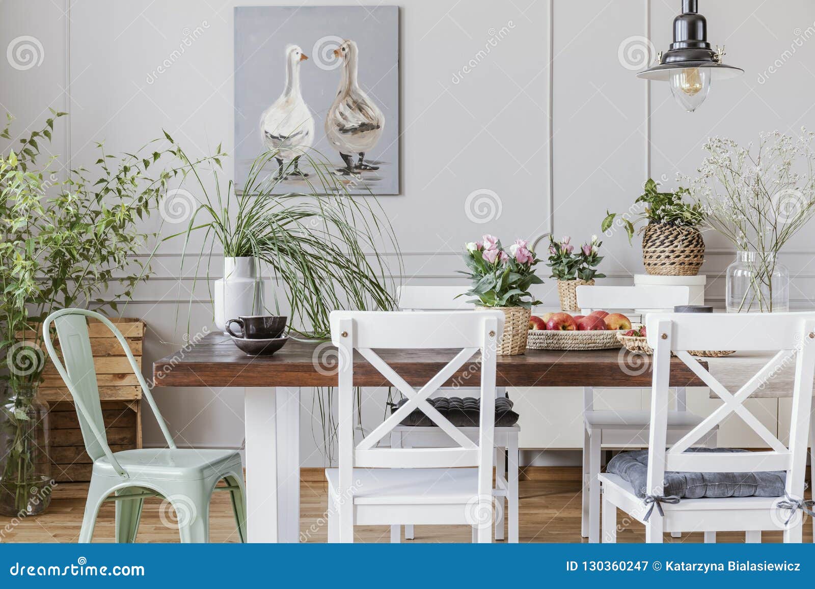 real photo of plants in a rustical dining room interior with a table, chairs, painting with ducks