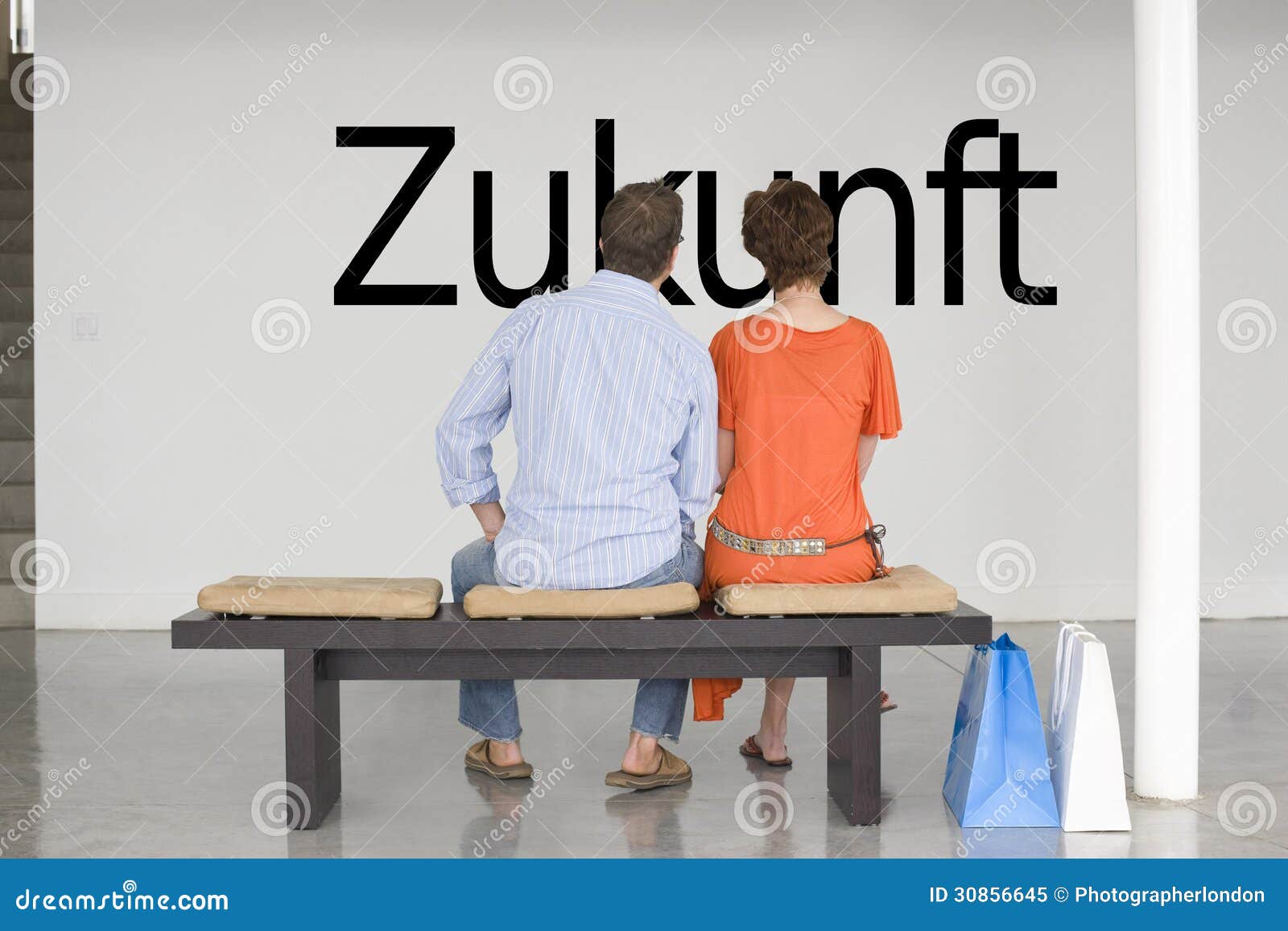 rear view of couple seated on bench reading german text zukunft (future) on wall