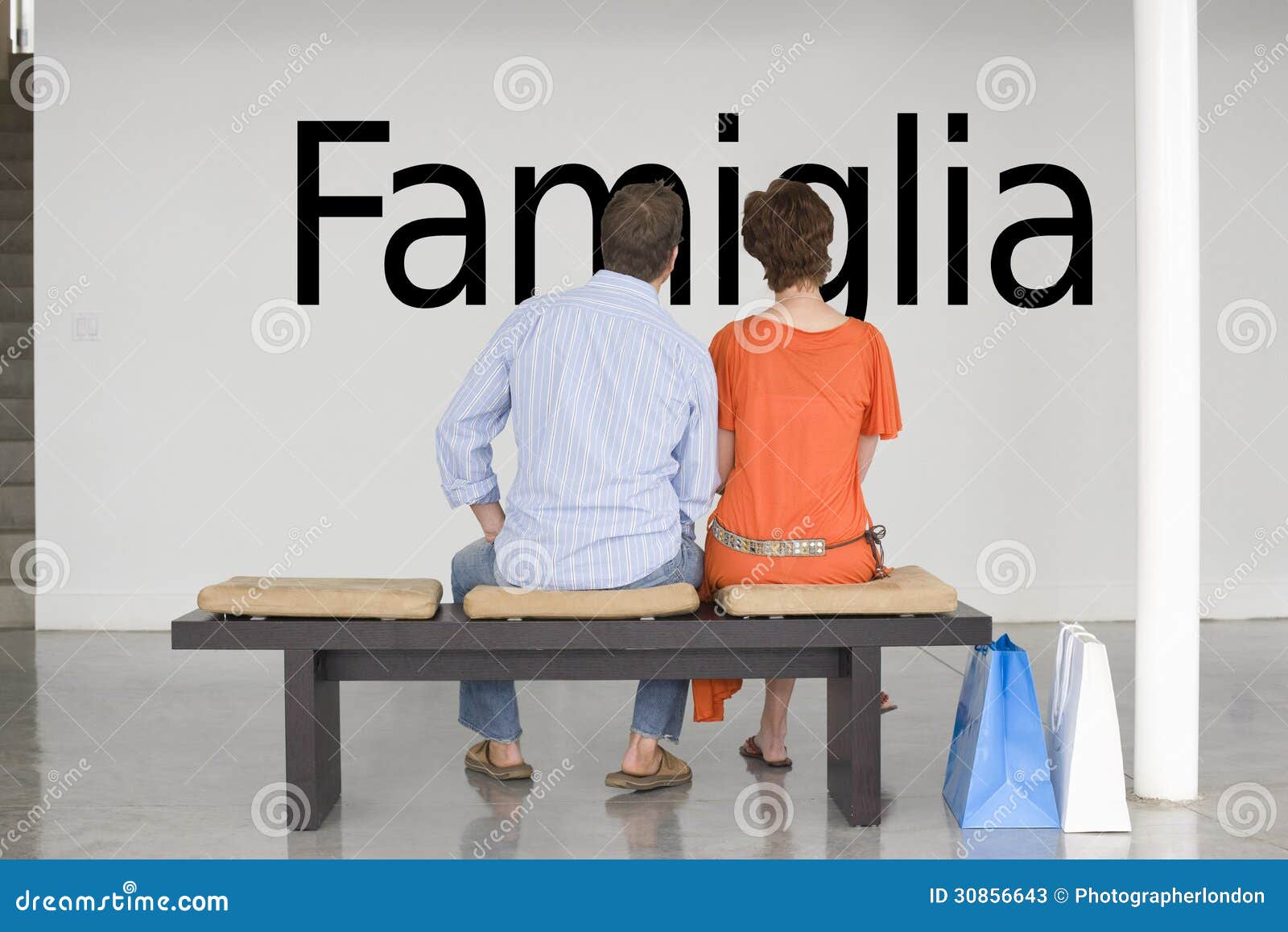 rear view of couple seated on bench reading italian text famiglia (family) on wall