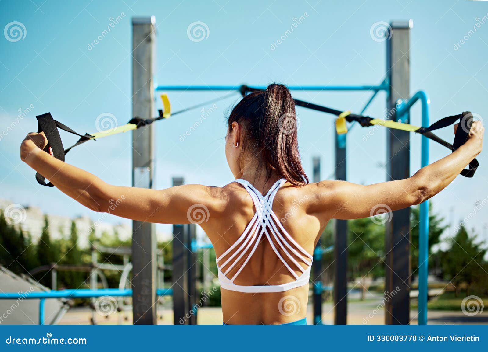 rear view of dedicated athlete utilizes trx bands at park, executing resistance exercise with precision. outdoor gym.