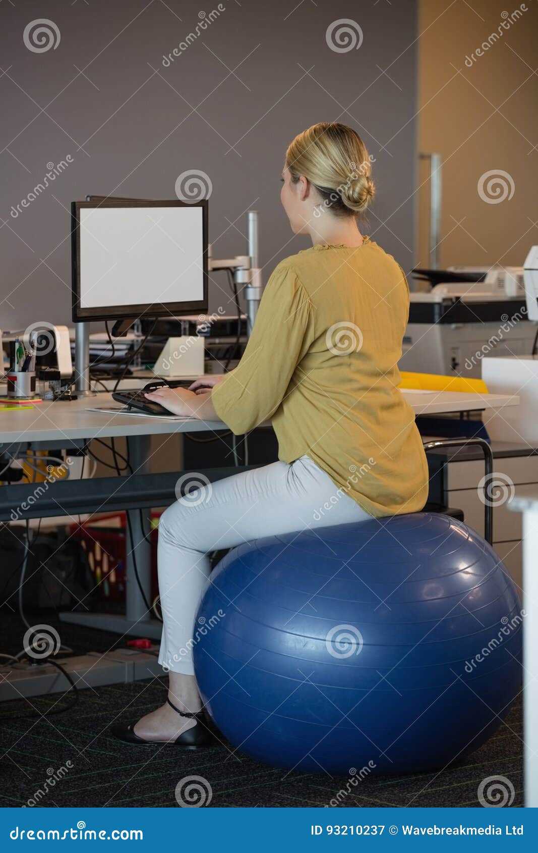 Rear View Executive Sitting On Exercise Ball While Working At Desk