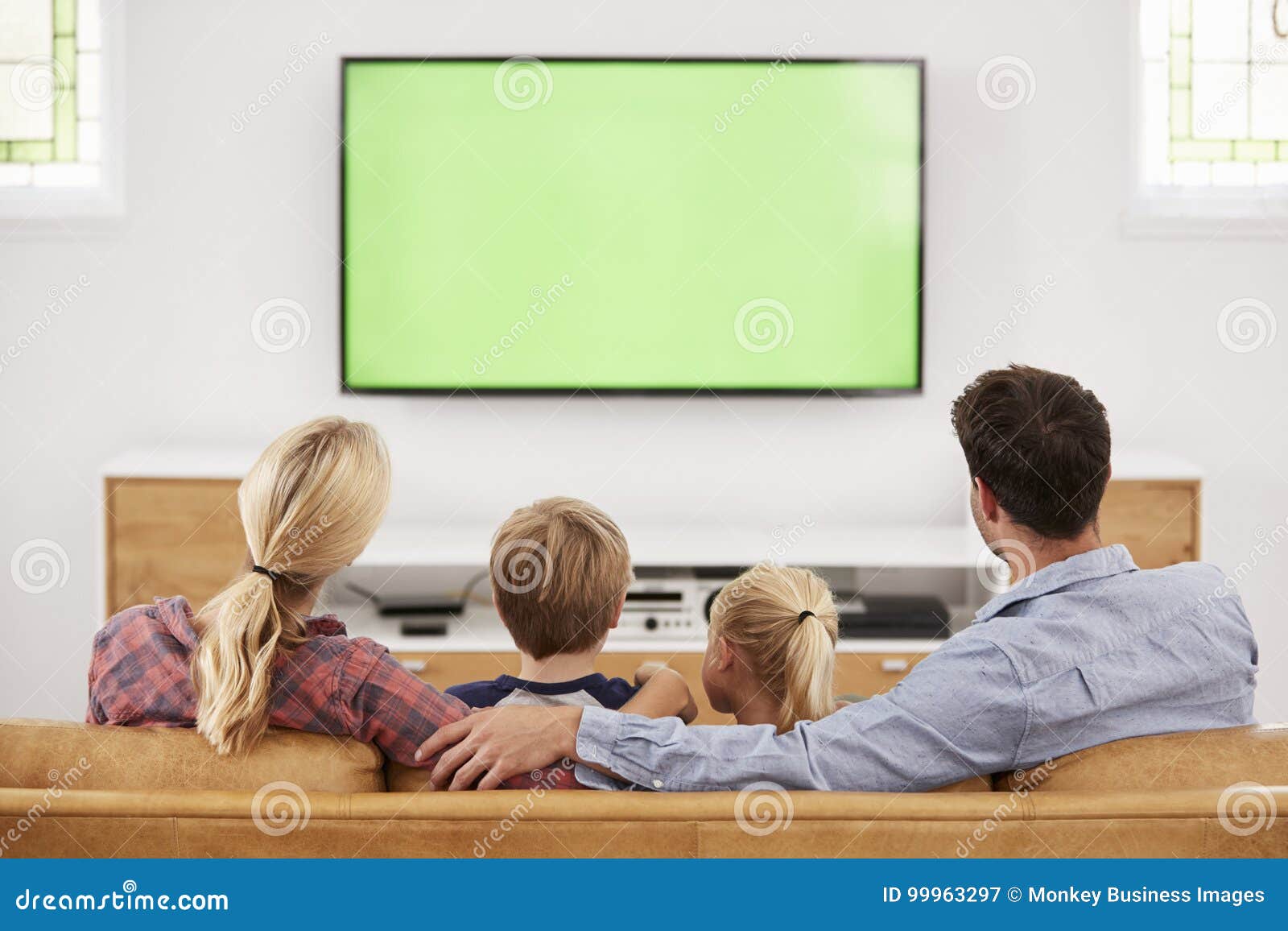 rear view of family sitting on sofa in lounge watching television