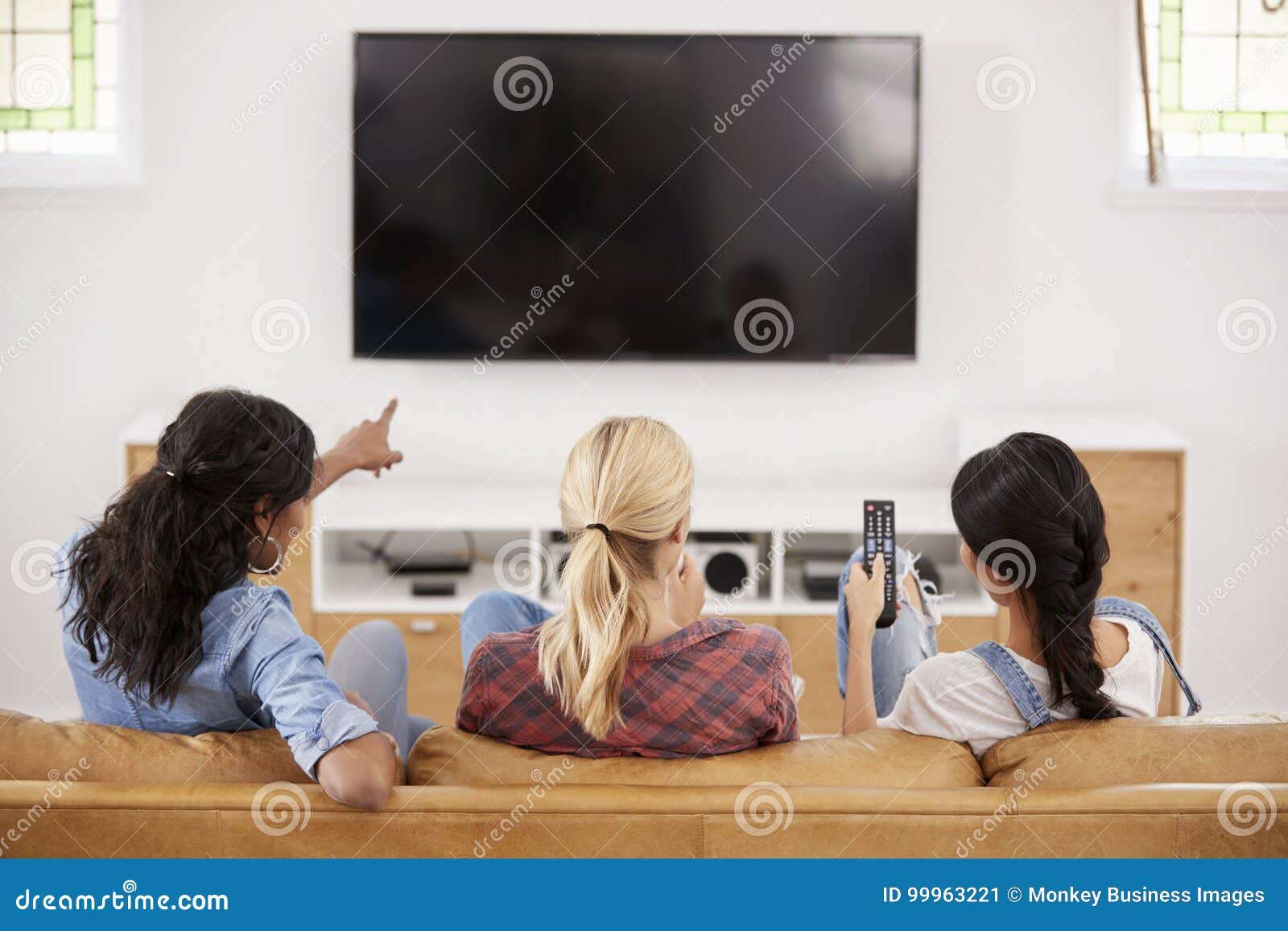 rear view of female friends sitting on sofa watching television