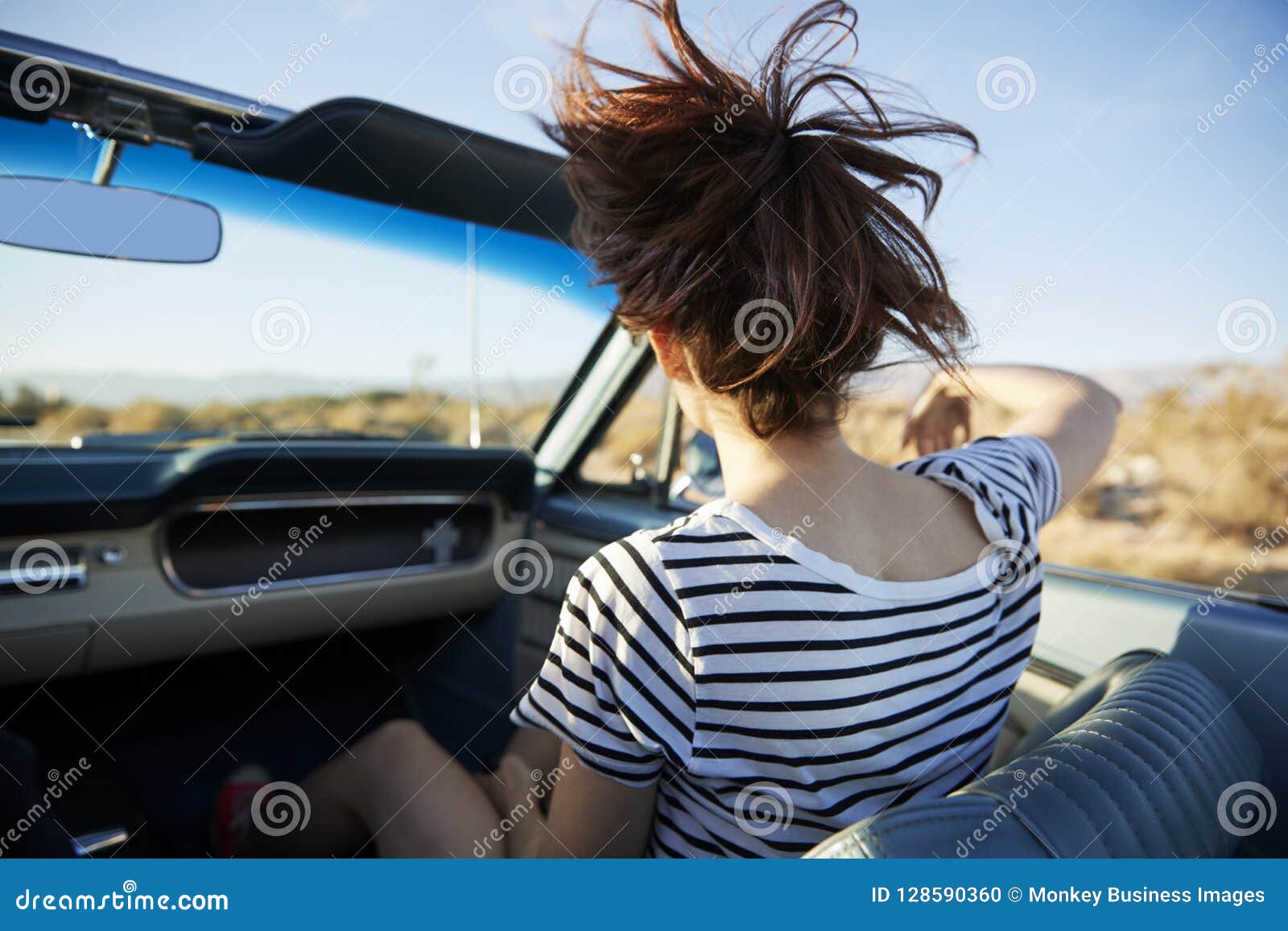 Smiling woman with water bottle driving a car, hair blowing in