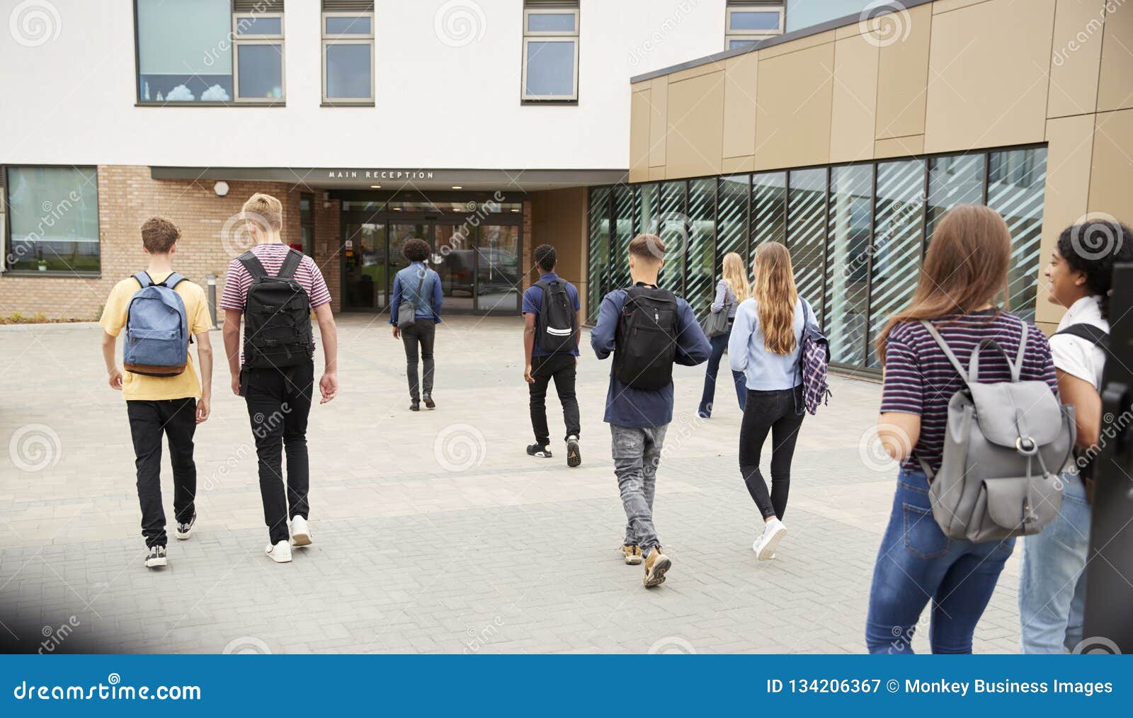 rear view of high school students walking into college building together