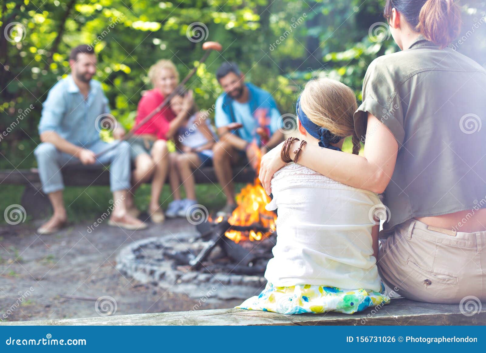 rear view of mother sitting with arm around daughter while camping at par