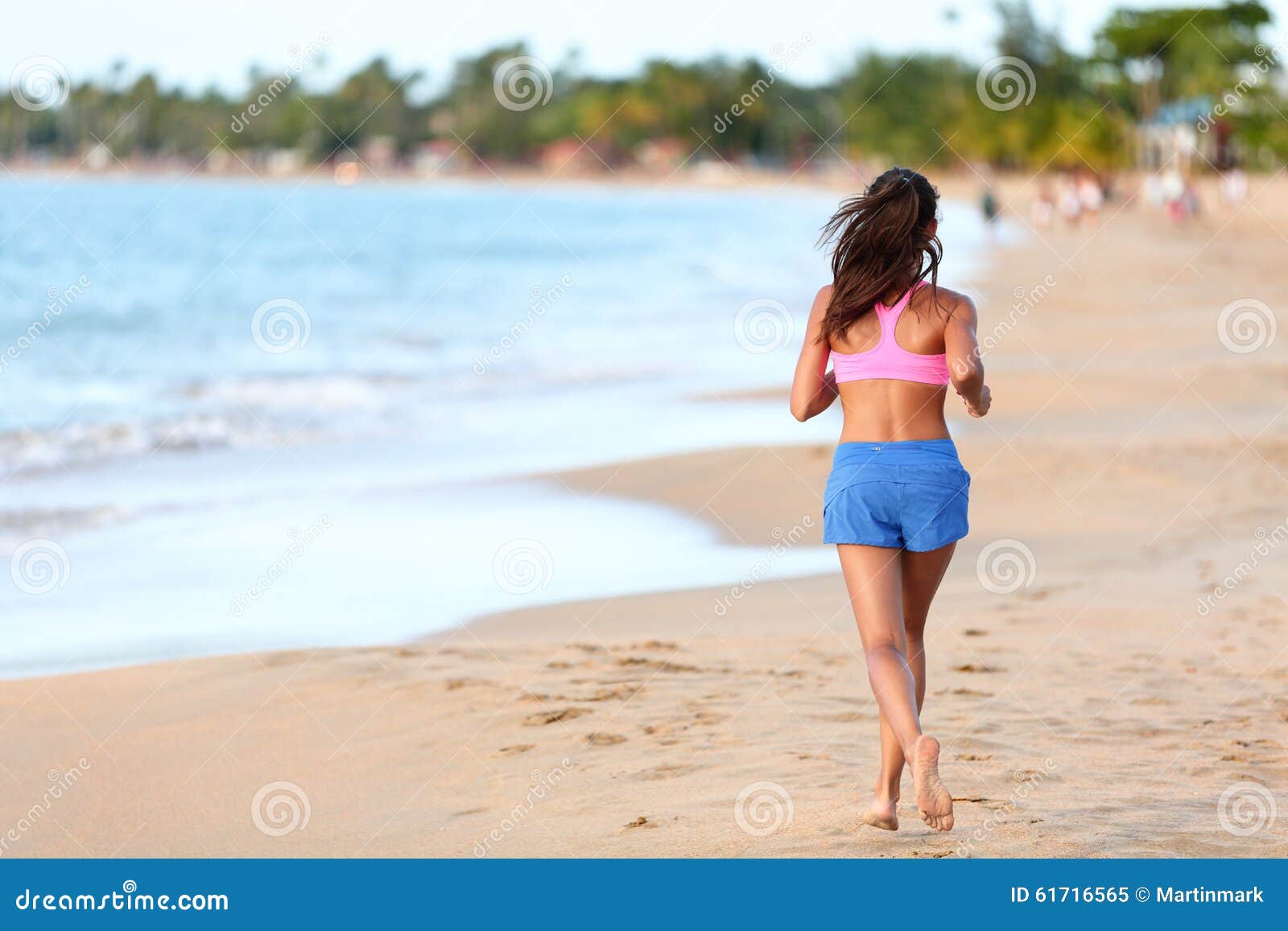 Rear View Of Sporty Woman Running On Beach. Young sporty woman running on beach. Full length rear view of determined female Runner in sports clothing. Jogger is exercising at sea shore during sunny day.