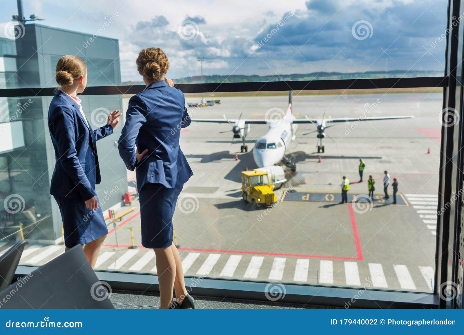 rear view of young attractive airport staffs looking at the plane through the window in airport