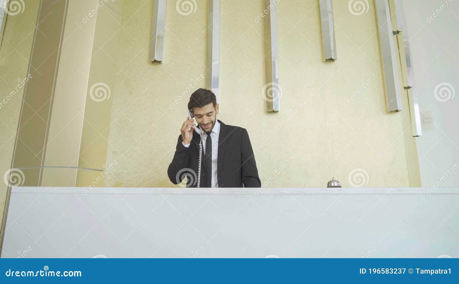 a receptionist or concierge man with uniform at front desk counter in lobby of hotel talking on the phone with guest about the