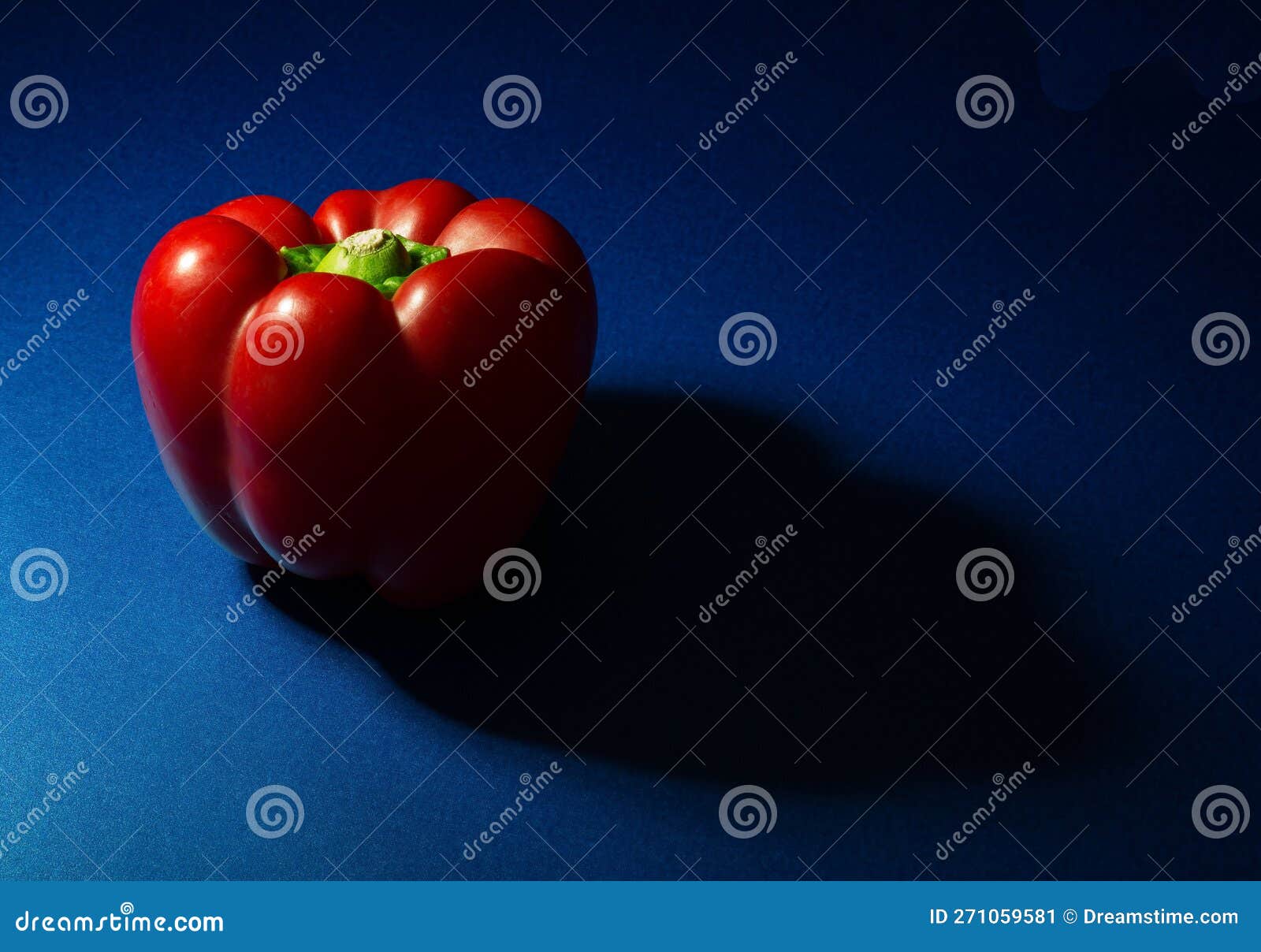 Red Bell Pepper Partially Lit with Shadow on a Blue Base Stock Image
