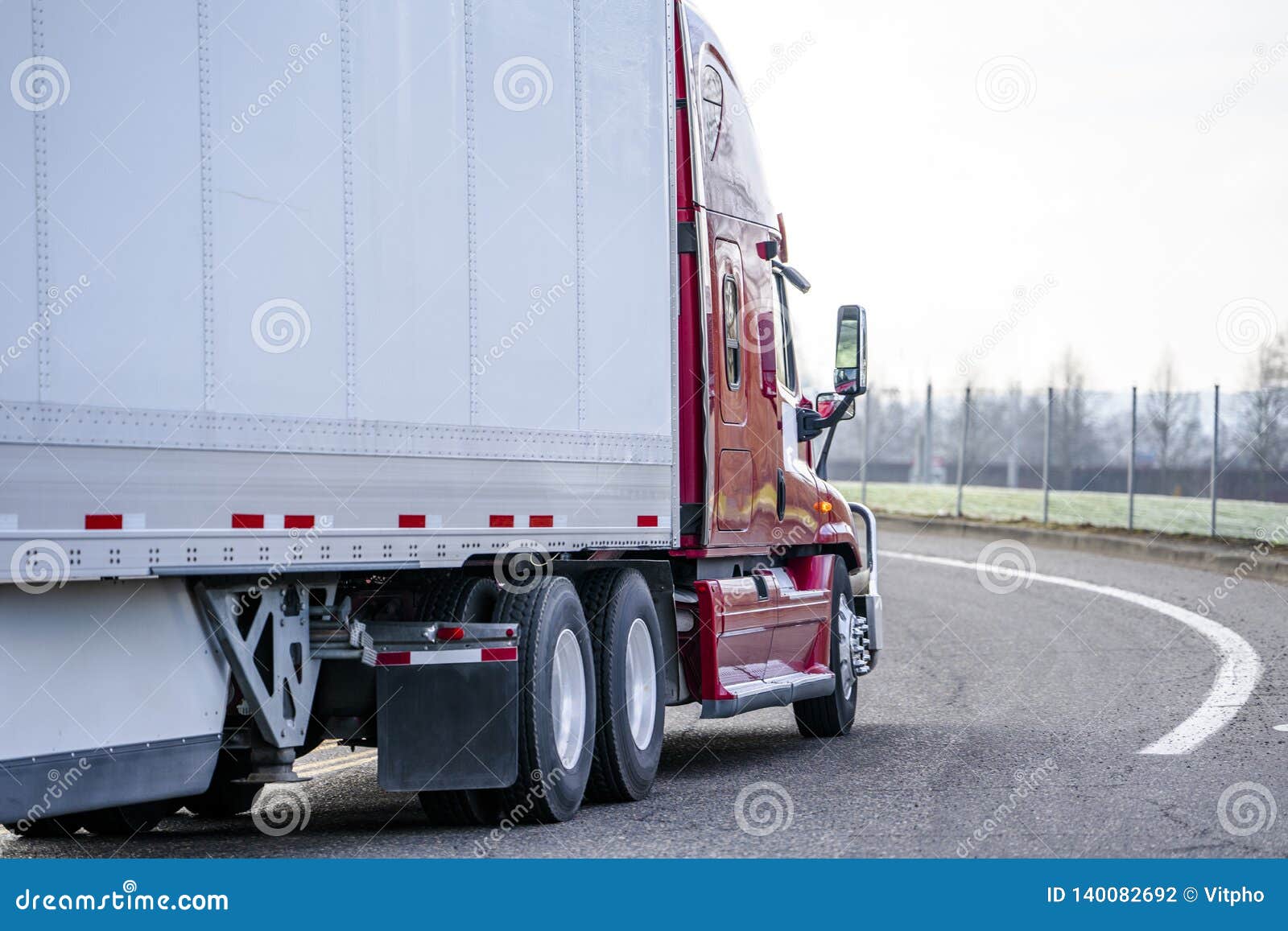 red big rig long haul semi truck transporting dry van semi trailer turning on the local road