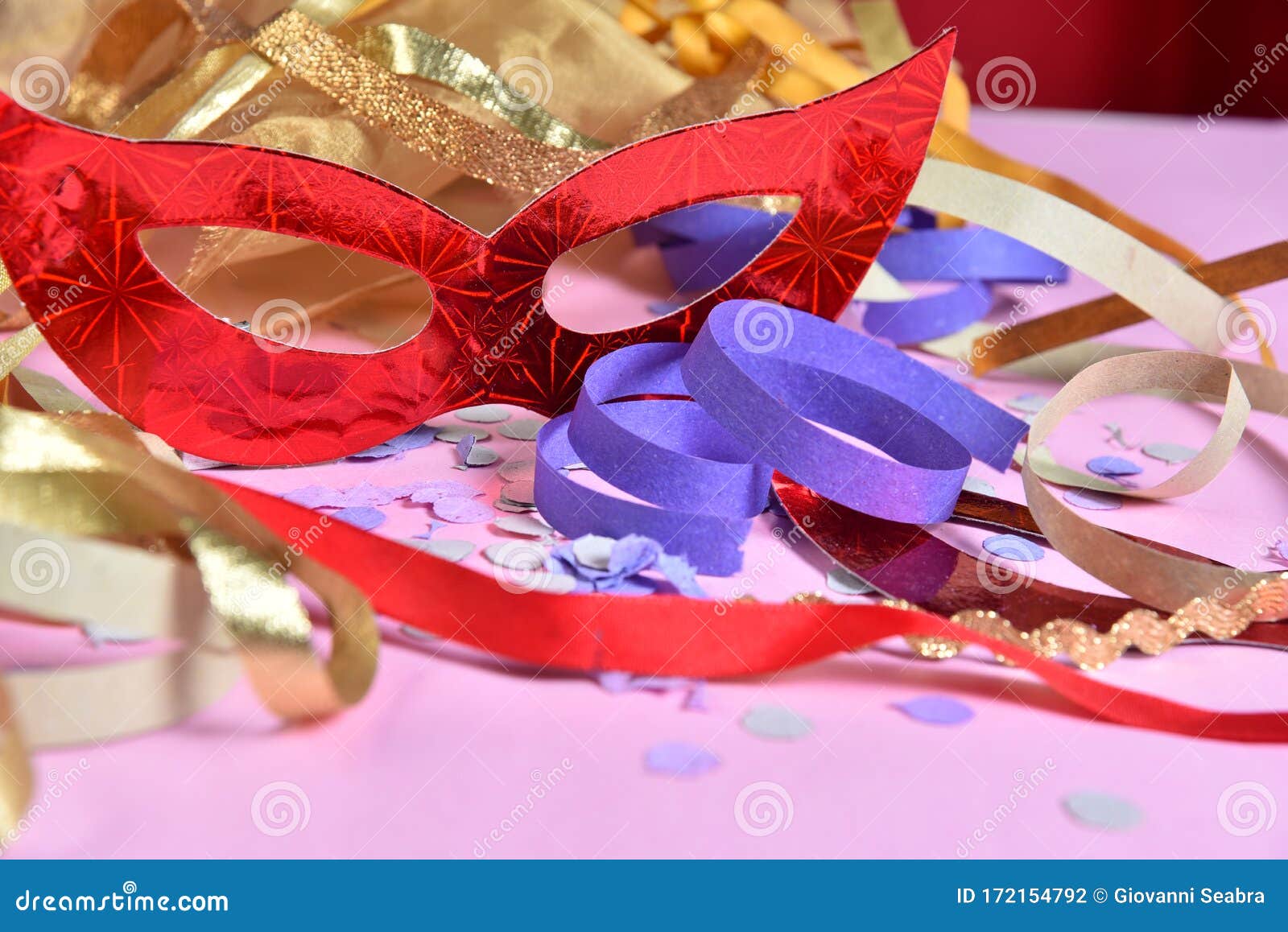 red carnival costume mask on colorful confetti necklace flowers and streamers with space for text