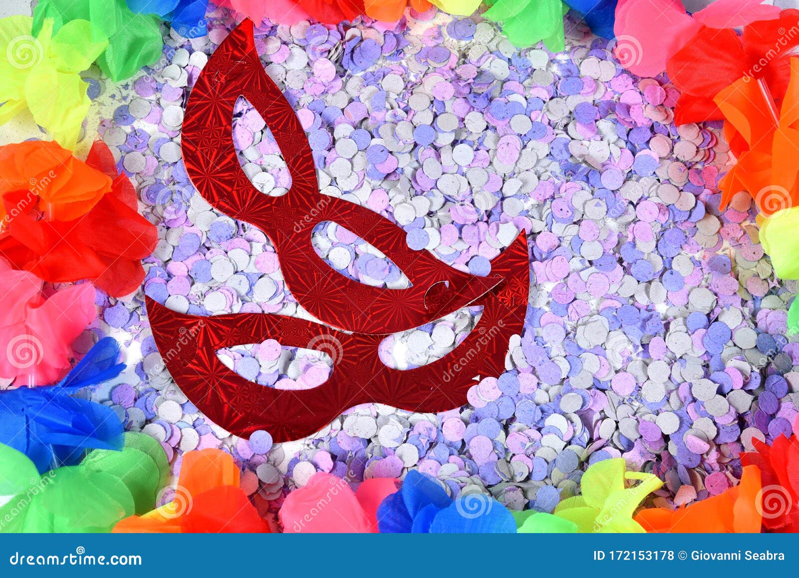 red carnival costume mask in colorful confetti and streamers on pink background with space for text