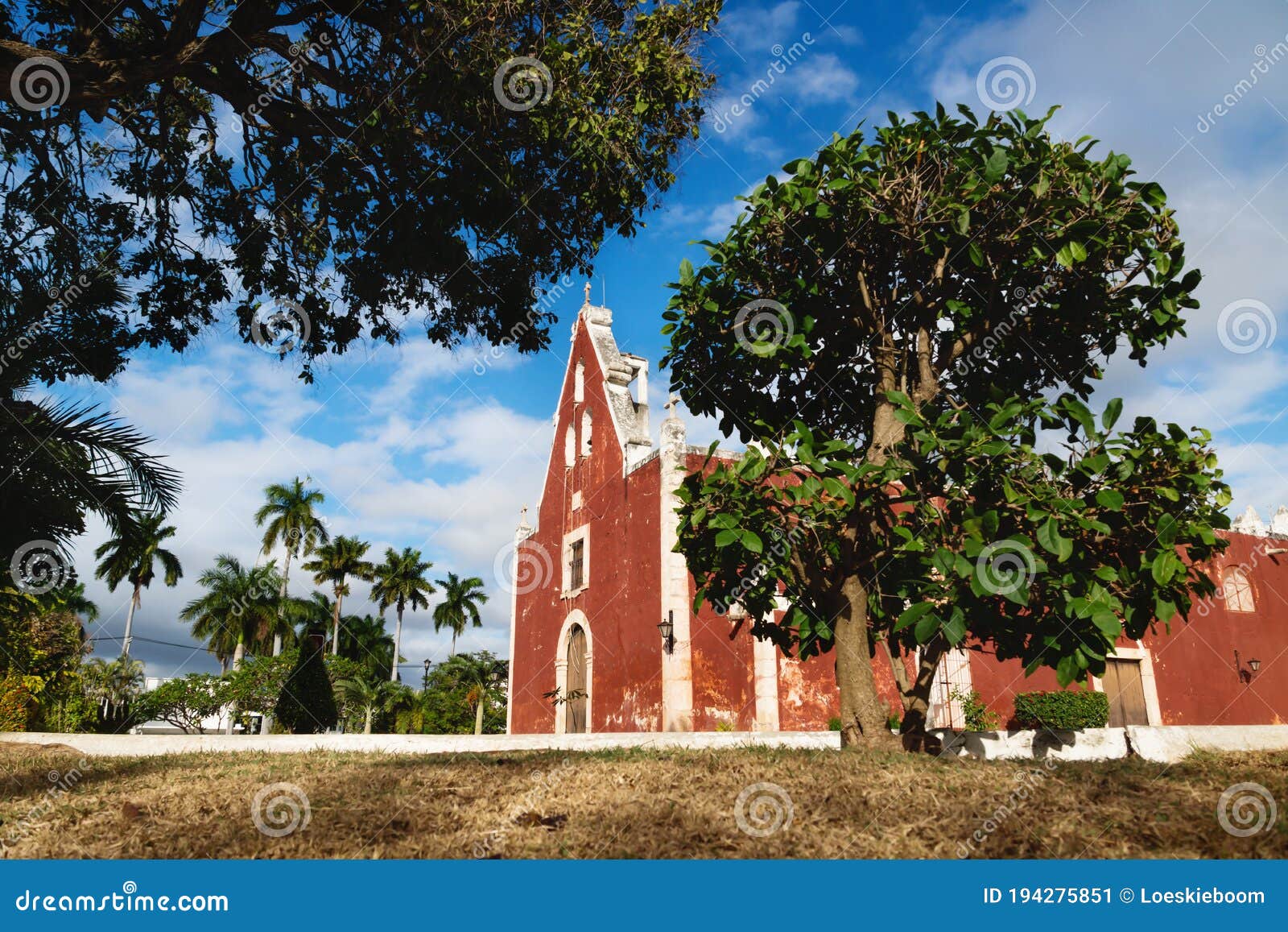 red colonial church itzimna in a park framed by trees, merida, yucatan, mexico