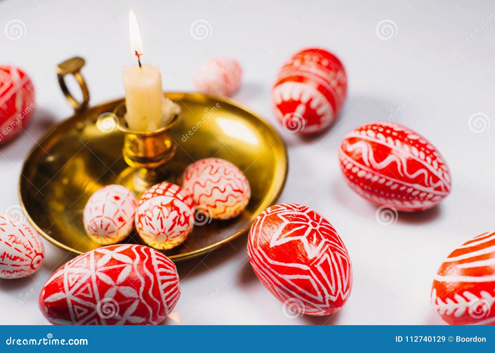 red easter eggs with folk white pattern on candlestick with burning candle on white background. ukrainian traditional eggs