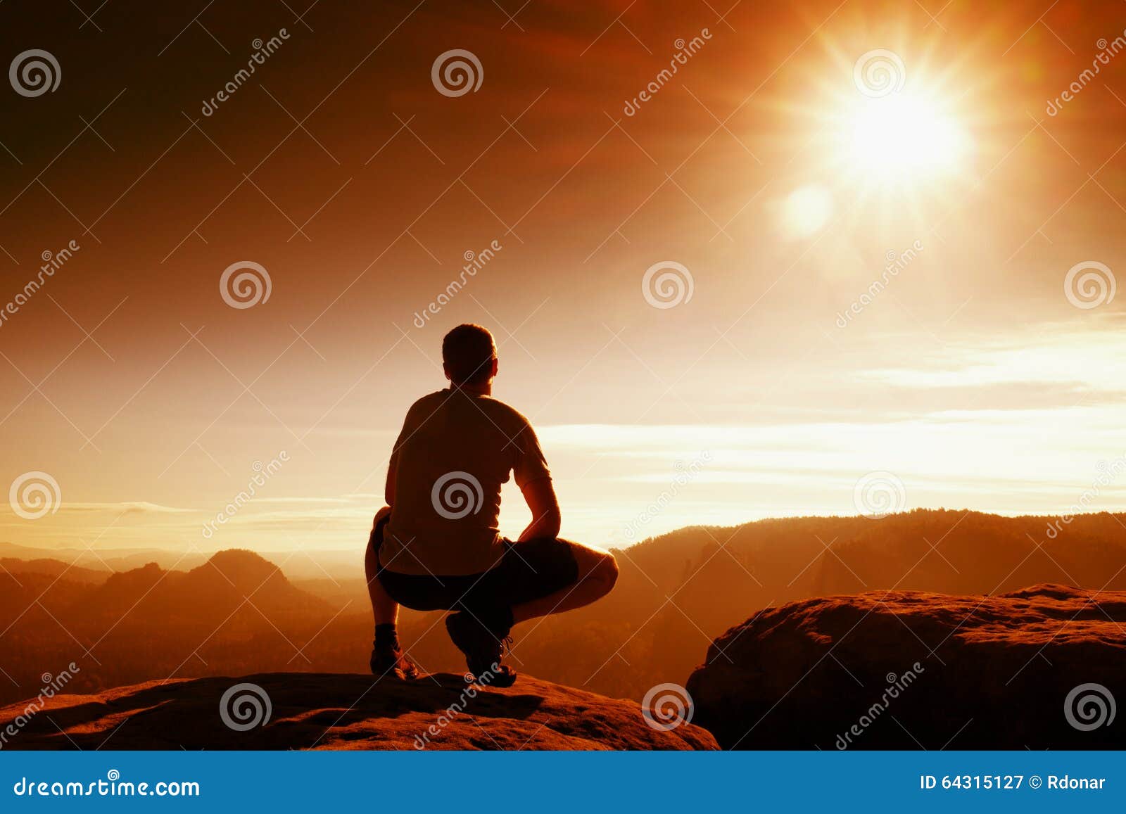 red filter photo. slim tourist in pants on the cliff of rock empire is watching down to valley. hot sun above.