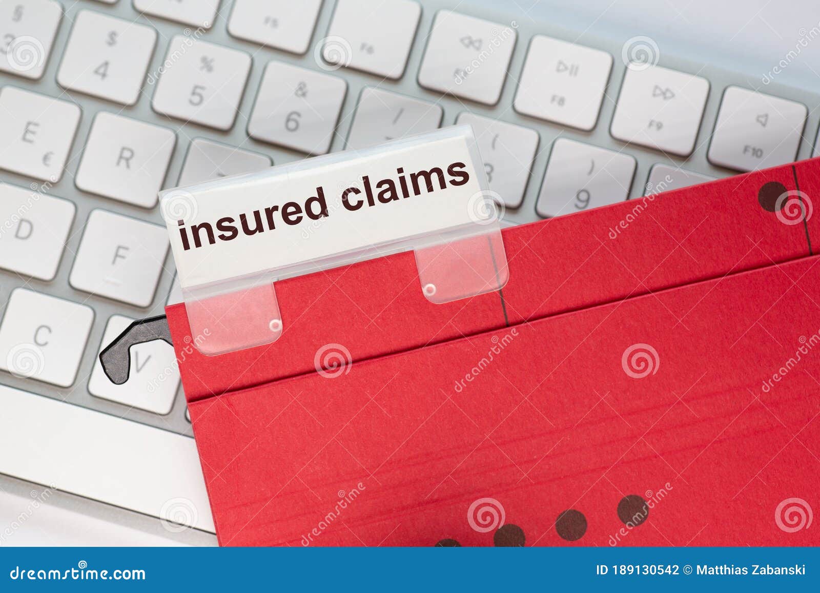 red hanging folder on a keyboard has a tab with the words insured claims on it