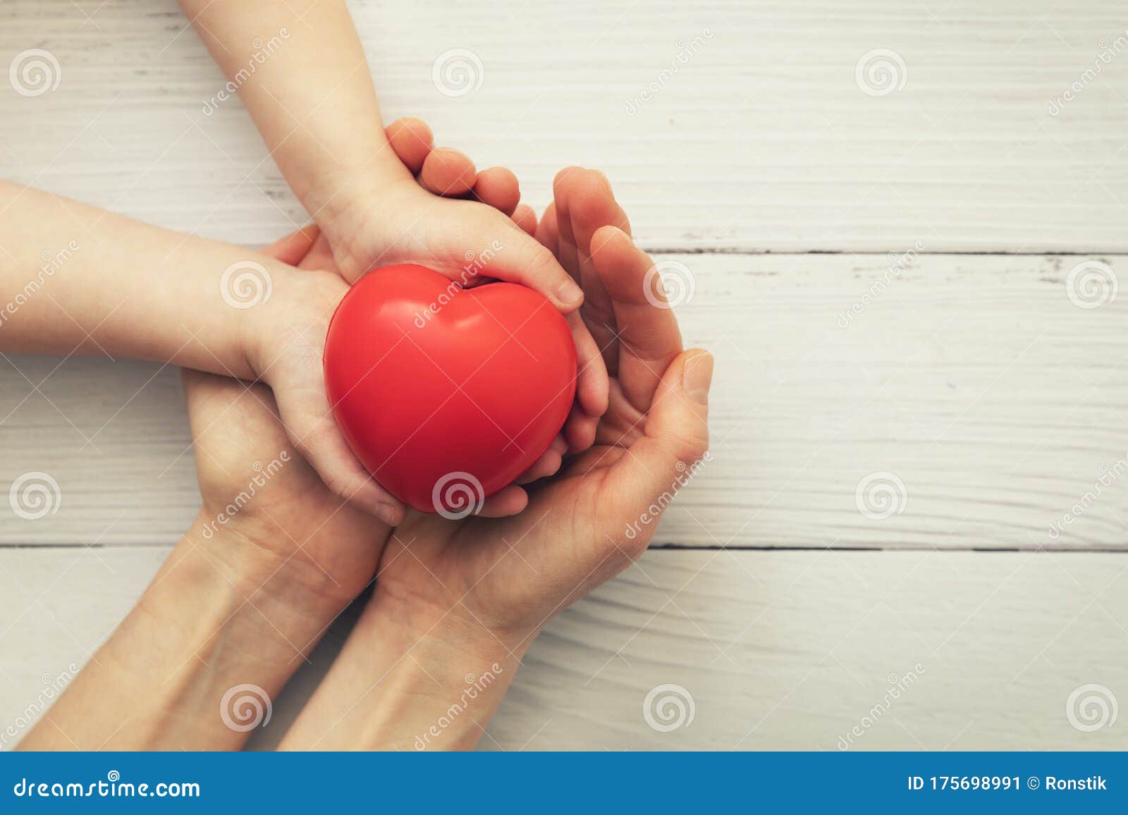red heart in child and mother hands on white wooden background. concept of love, charity, empathy