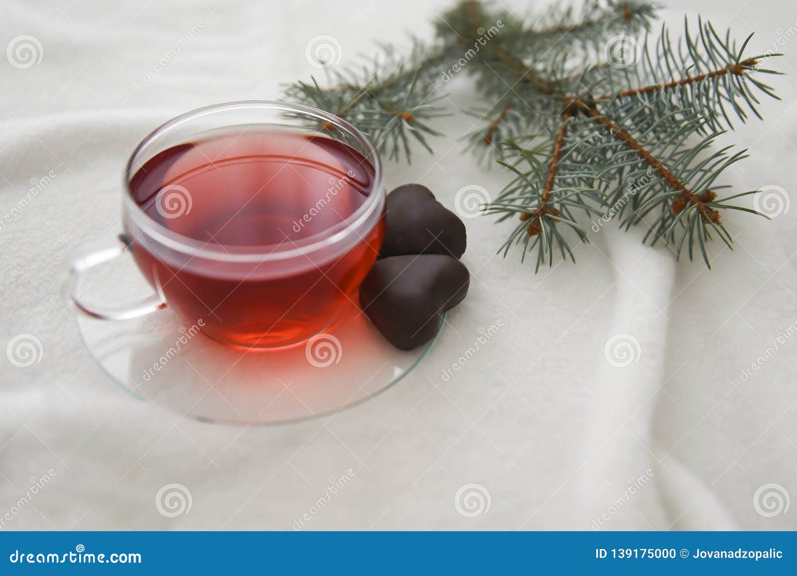 Red hot aromatic tea made from forest fruits or herbal or apples or red fruits in the glass cup on a white blanket. Red hot aromatic tea made from forest fruits or herbal or apples or red fruits in the glass cup on a white blanket with two heart-shaped chocolate cookies. Tea for two, Valentine`s Day..