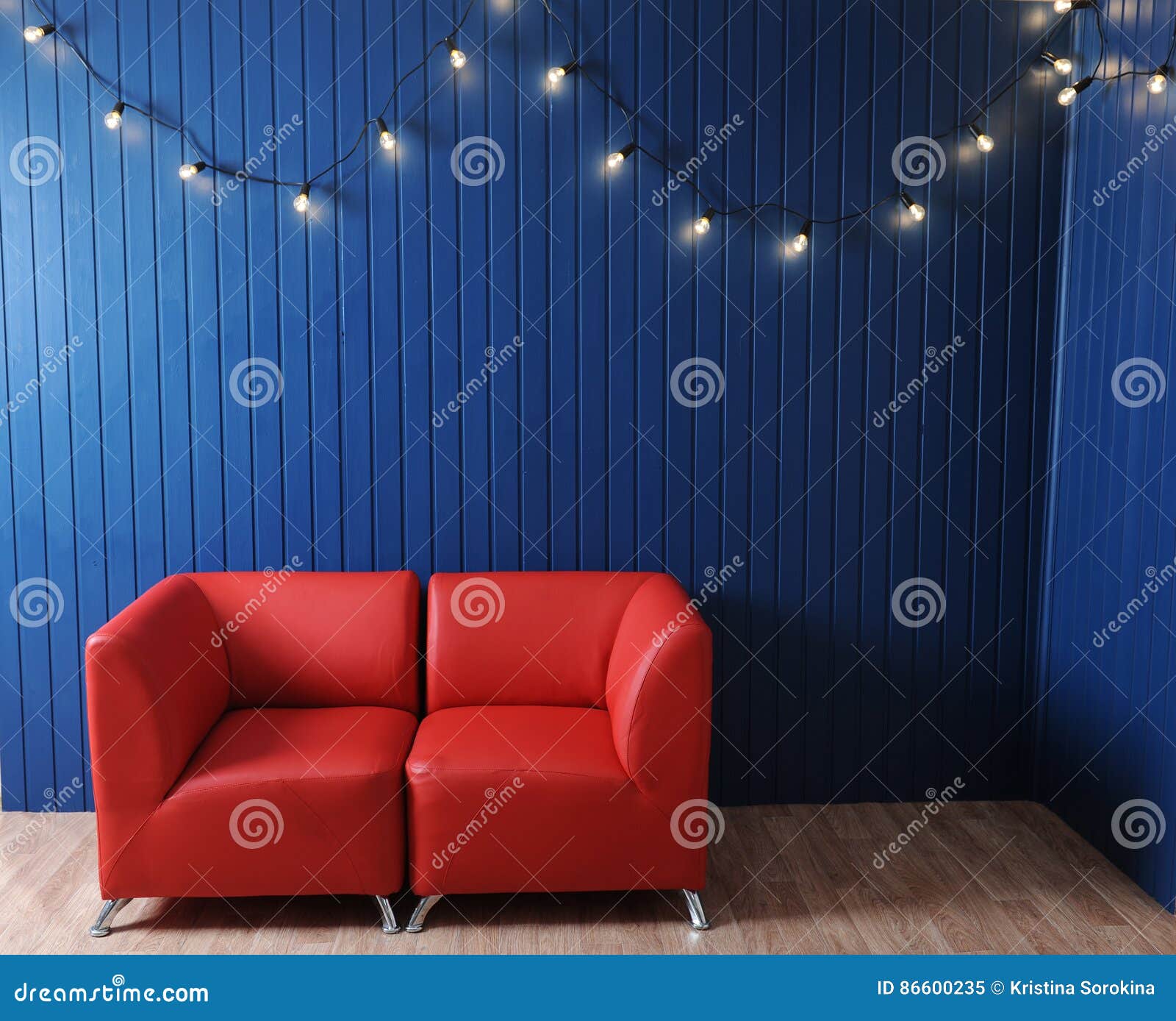 Red Leather Sofa on a Background of Blue Wall with Retro Garland of Light Bulbs. Texture for the