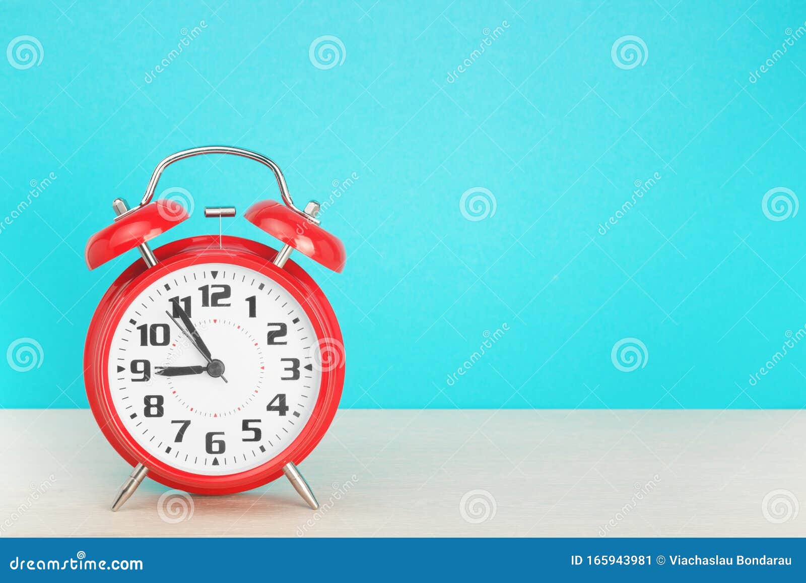 red retro alarm clock with five minutes to nine o`clock, on wooden table on a blue background