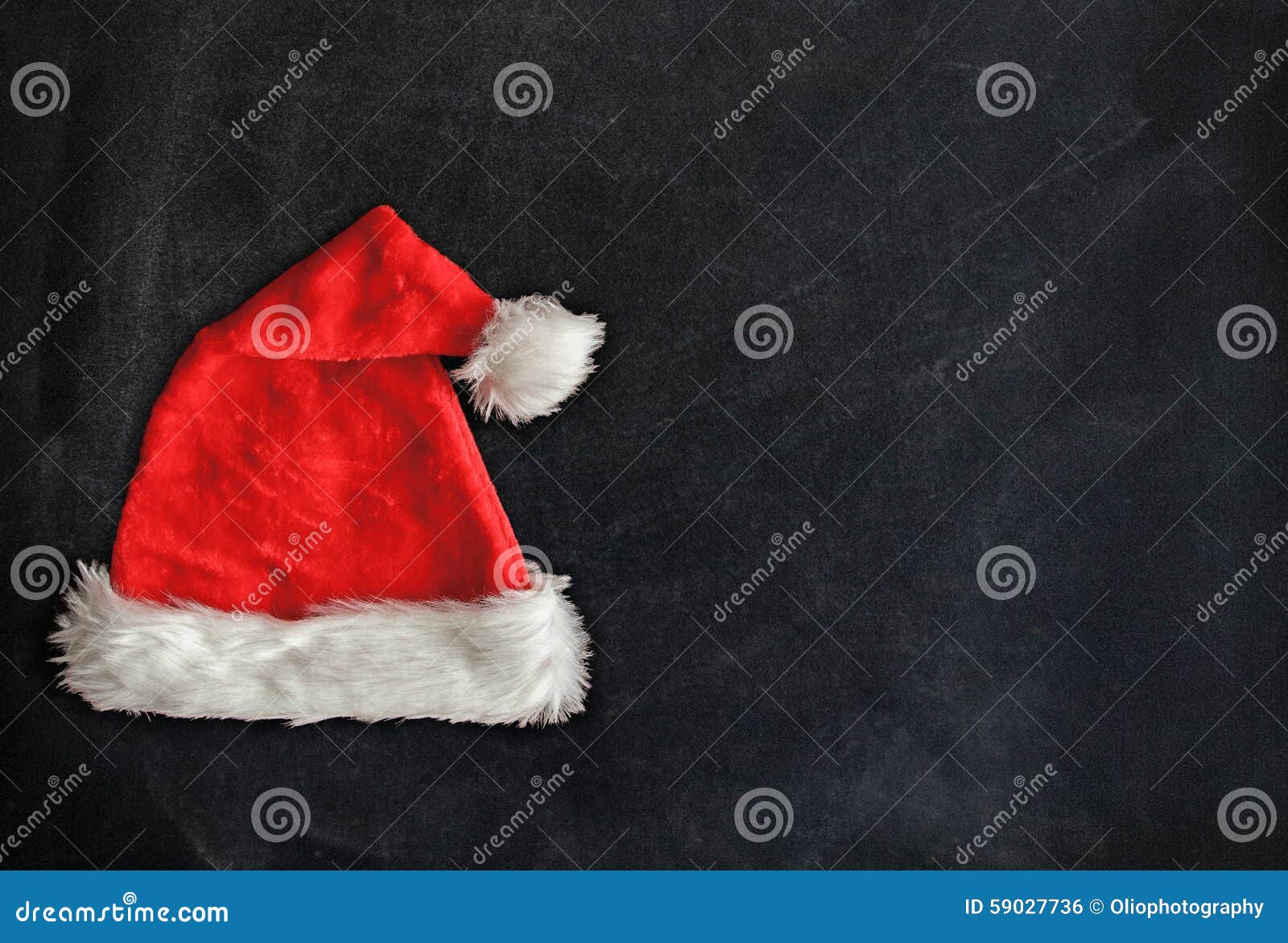 Red santa hat with white fur trim on blackboard. Copy space for a Christmas greeting.