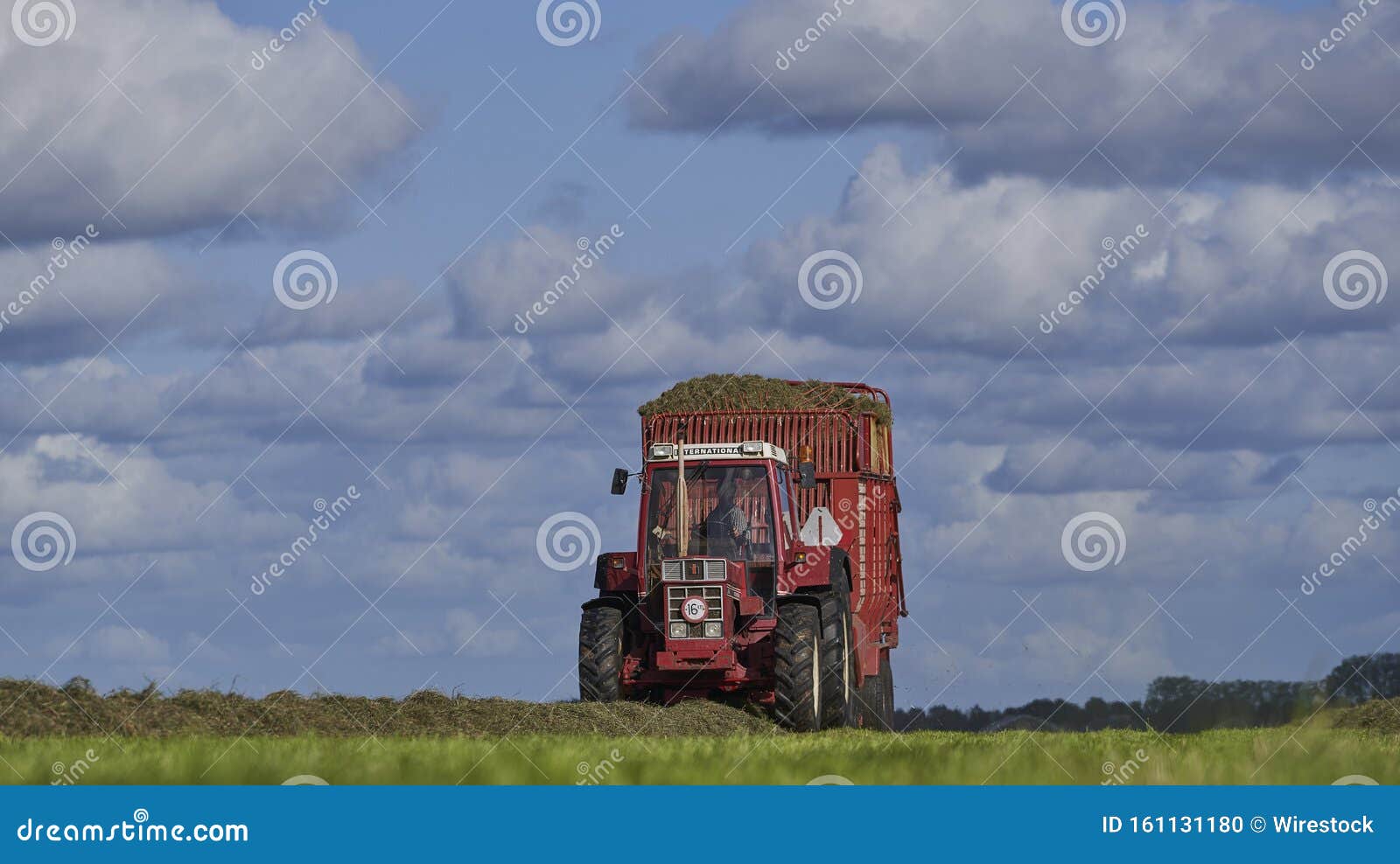 Red Tractor Driving on a Farm Field with a Blue Cloudy Sky in the