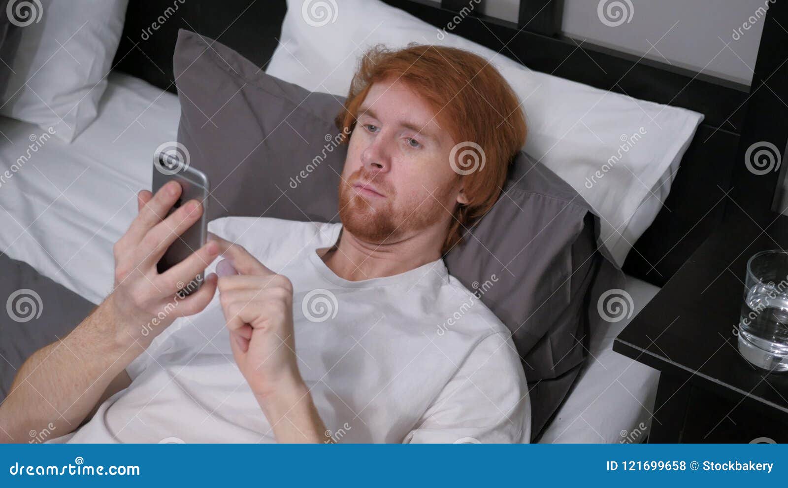 Redhead Man Lying in Bed Using Internet on Smartphone Stock Photo ...