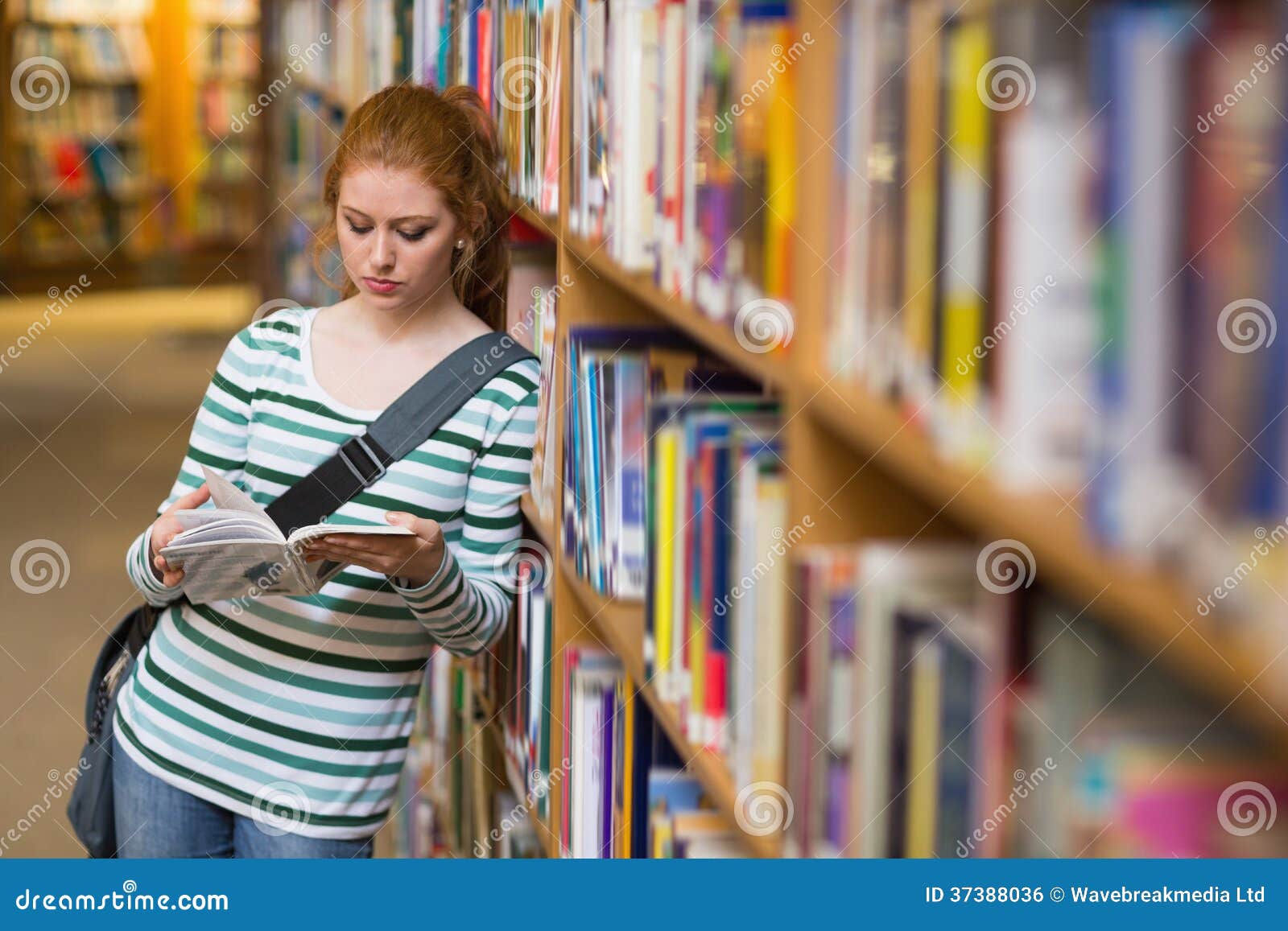 redhead student reading book leaning on shelf in library